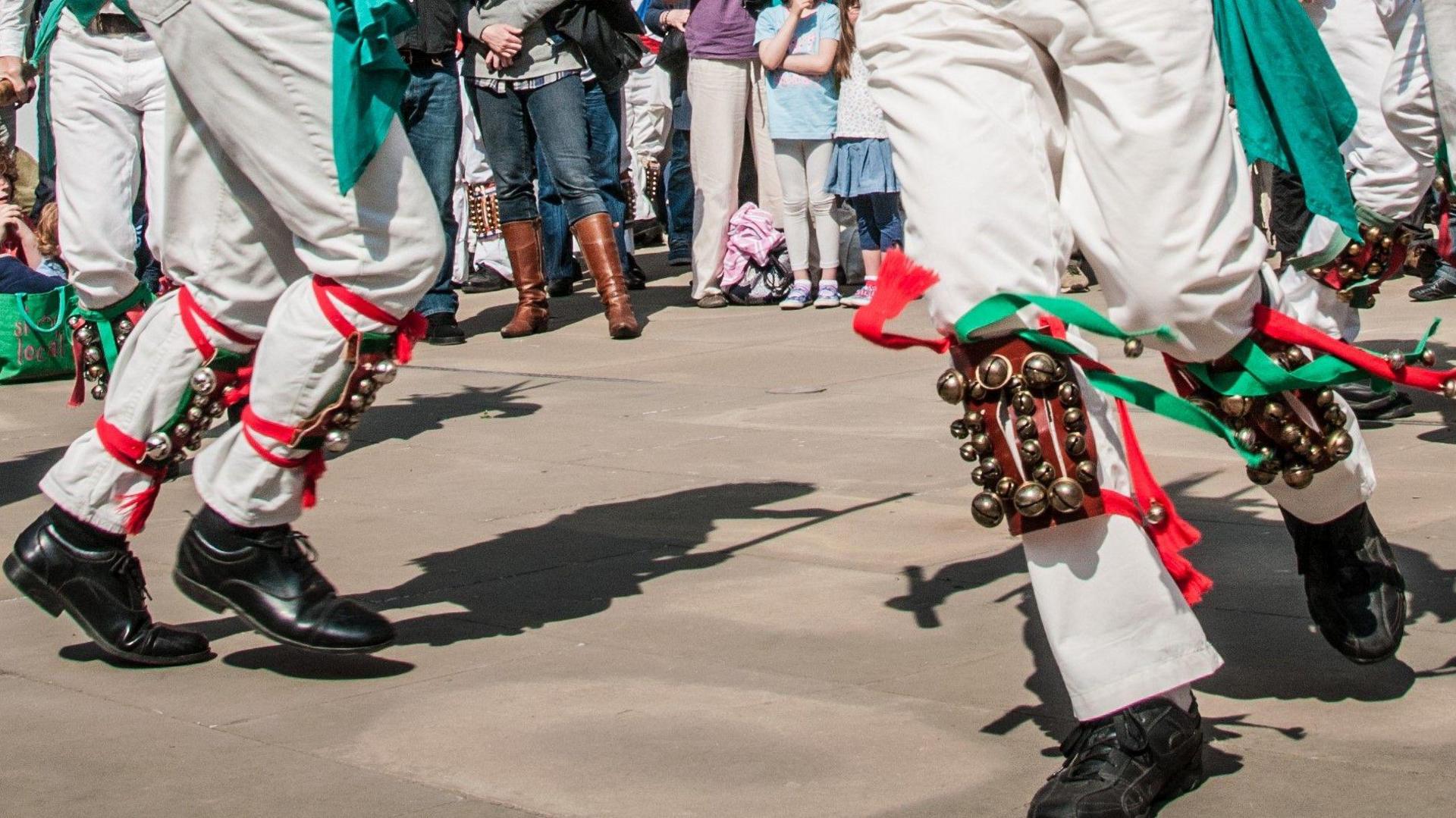 A group of Morris dancers wearing white trousers with bells attached to the knees along with red and green ribbons.