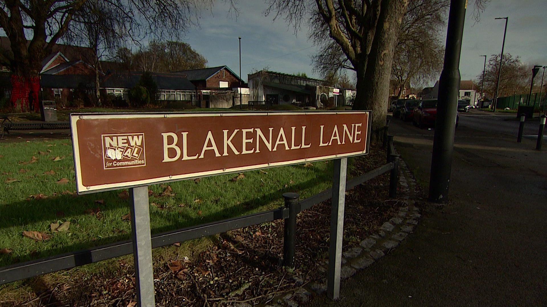 A brown road sign with white lettering on Blakenall Lane. The sign also feature the 'new deal for communities' logo.