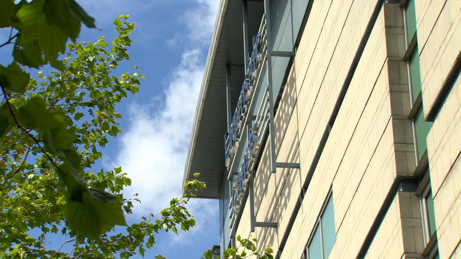 One wall of Belfast Crown Court seen from outside on a sunny day. A tree is close to the wall and a sign says Laganside Courts