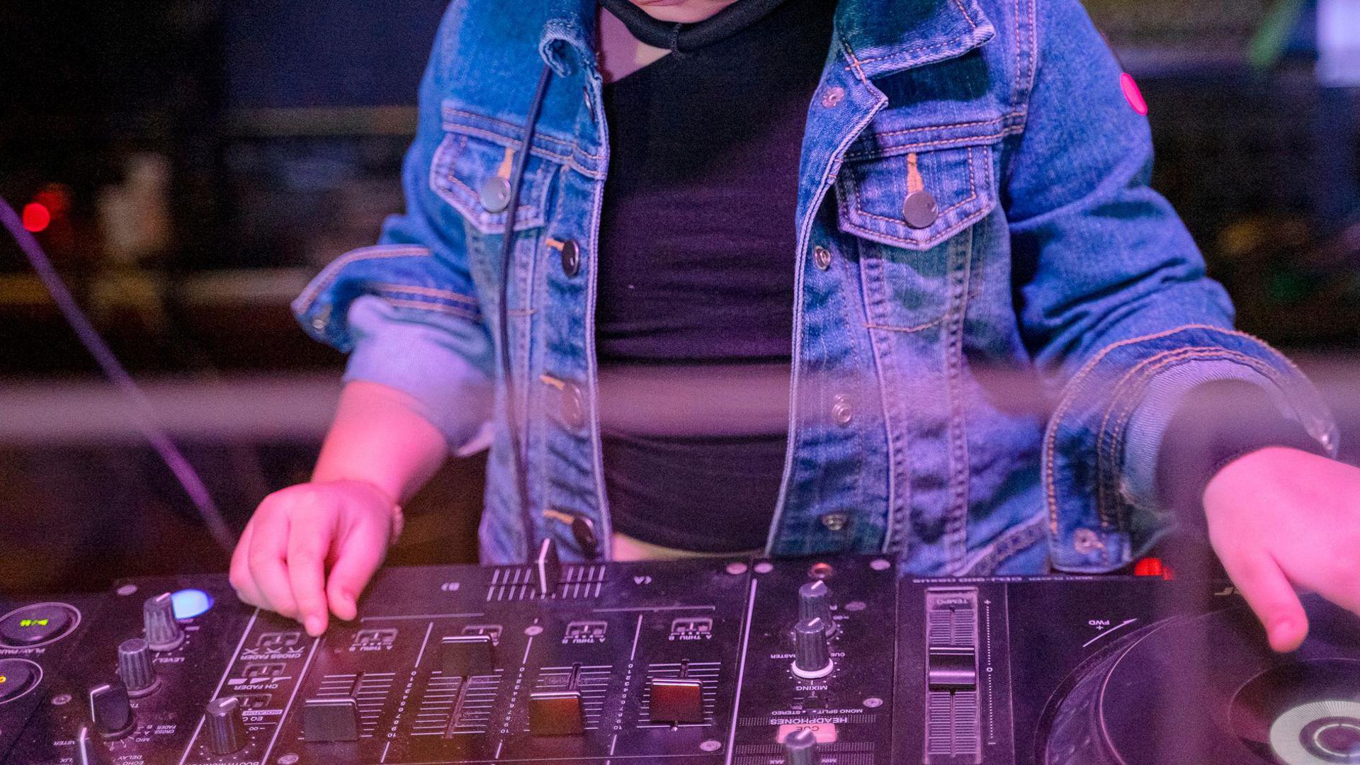 Stock image of a young girl, wearing a denim jacket, operating DJ decks.