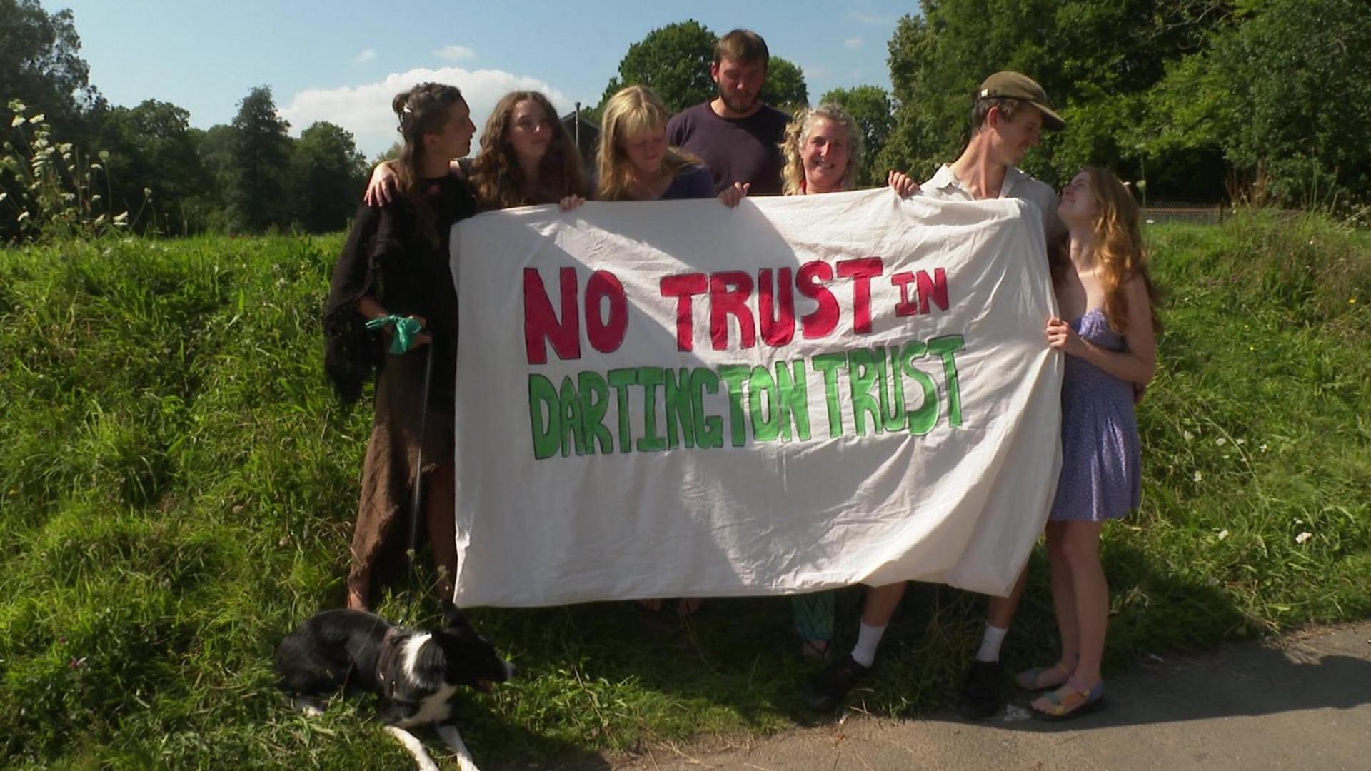 Close up of Schumacher College students holding a sign which reads 'no trust in Dartington Trust'