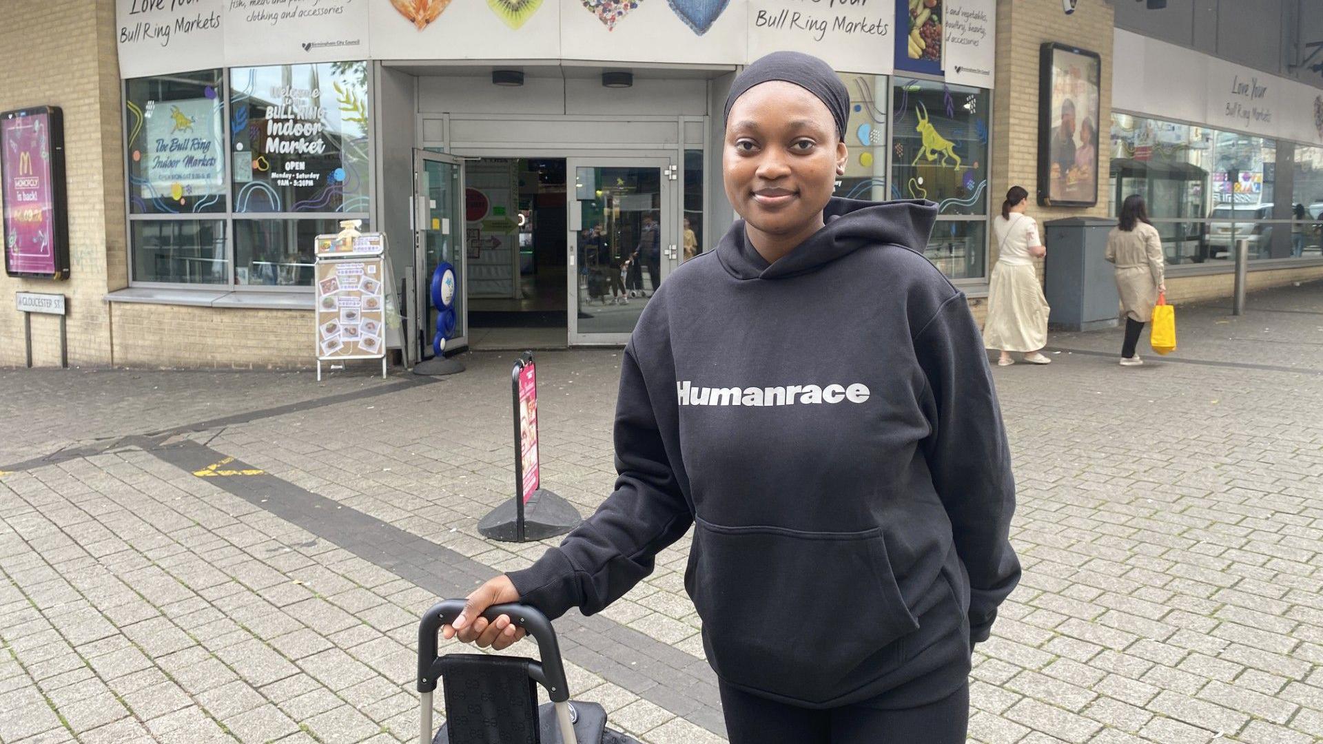 Ney Colonia outside the Bull Ring Indoor Market. She is wearing all black and holding a shopping trolley. 