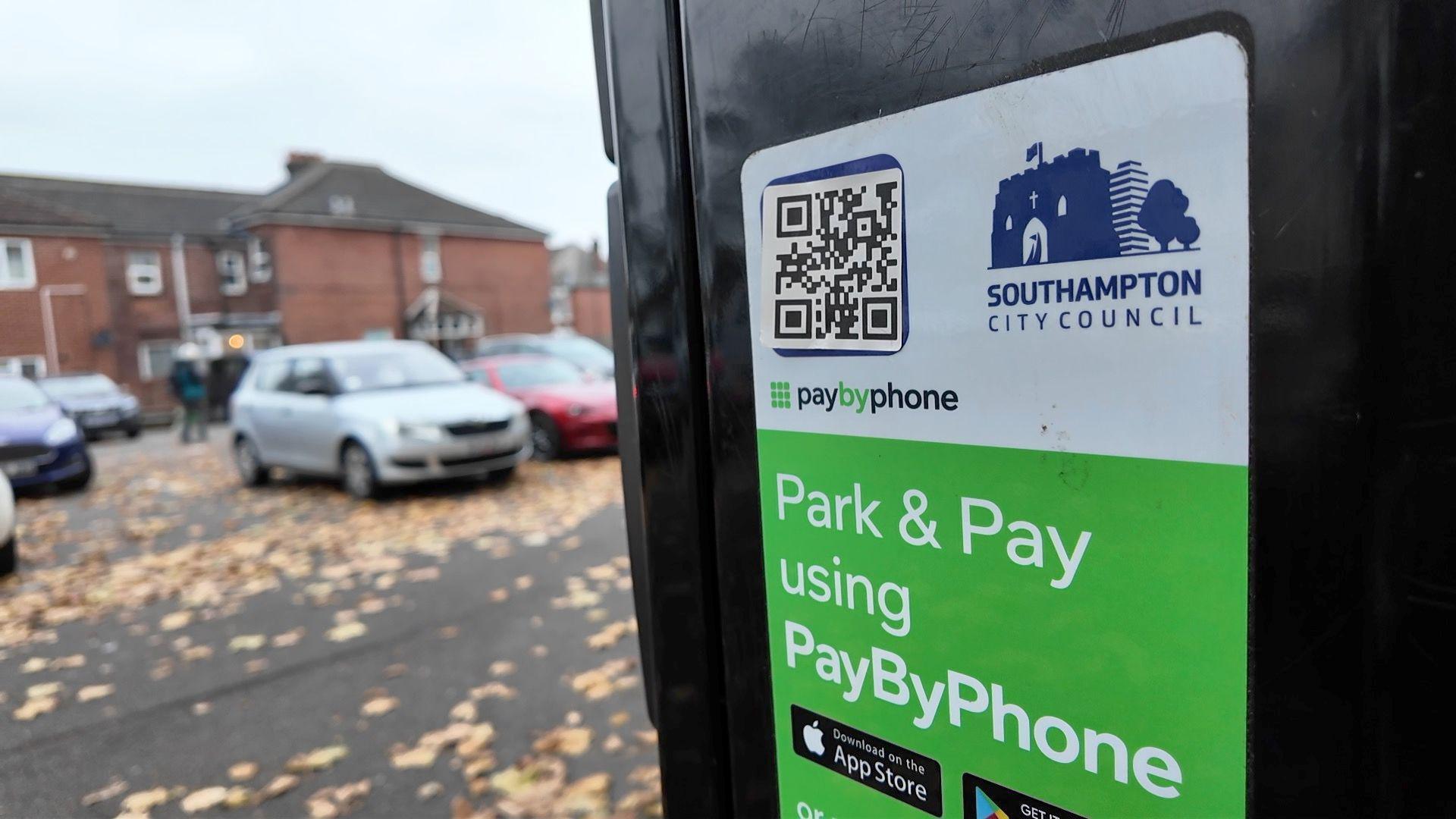 A parking meter with a Southampton City Council logo alongside a paybyphone logo and there is also a QR code sticker stuck to it with cars parked in the background.