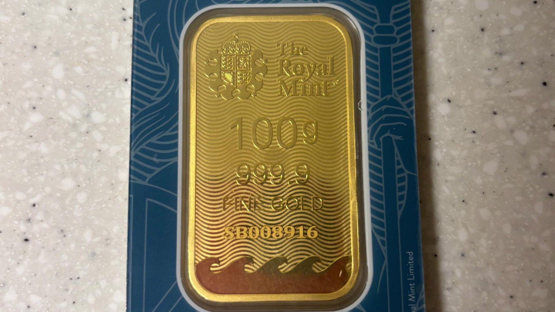 A gold bar from the Royal Mint sealed in packaging. It says the Royal Mint on it as well as the weight of 100g.