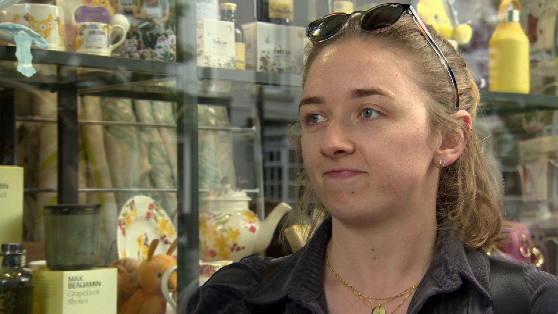 Katie Lewis stands in the shop in front of a glass display case