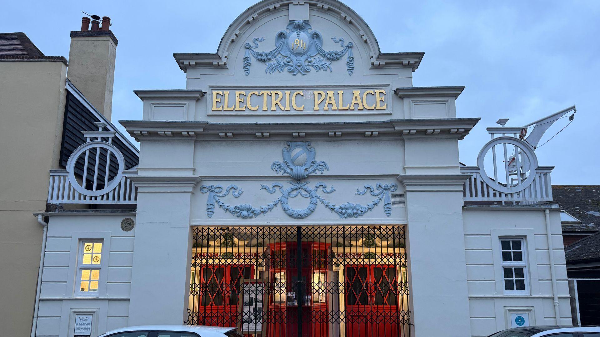 The outside of the Electric Palace cinema. It is a white building with black gates in front of red doors. The name of the cinema is at the top of the building in gold lettering.