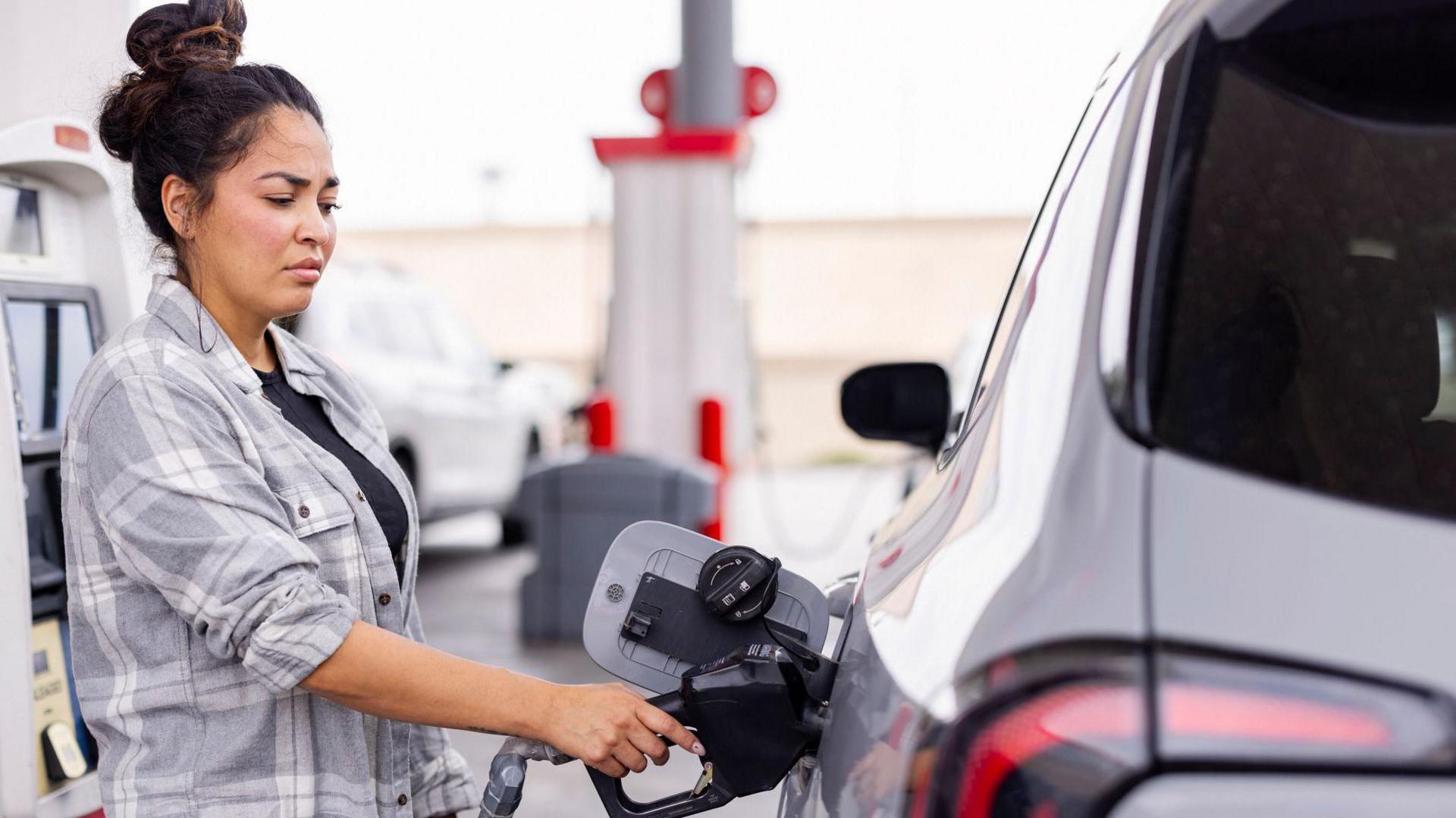 Woman wearing a grey shirt fills up her car at a gas station