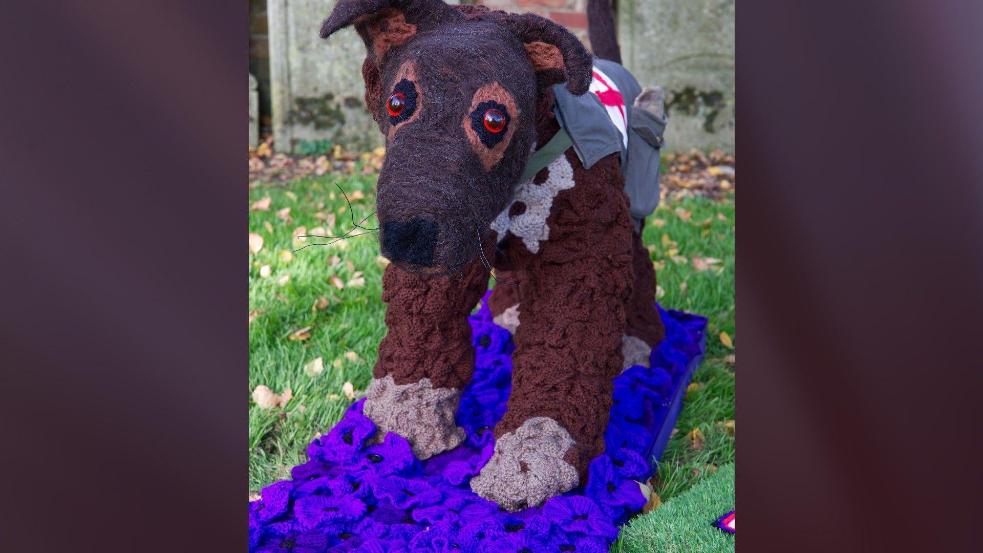 A brown knitted dog decorated with brown and purple flowers 