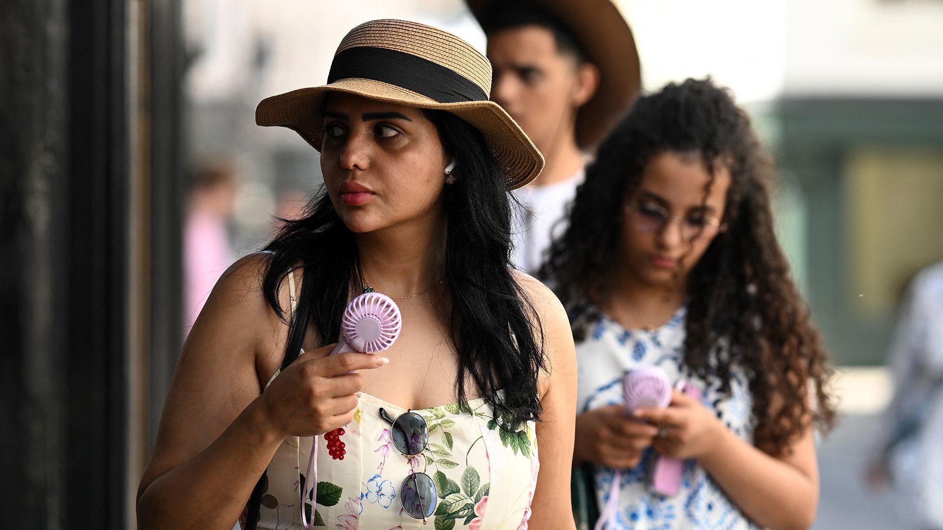 People walk down a street carrying portable electric fans and looking hot, while wearing summer clothing, in York on 24 June.