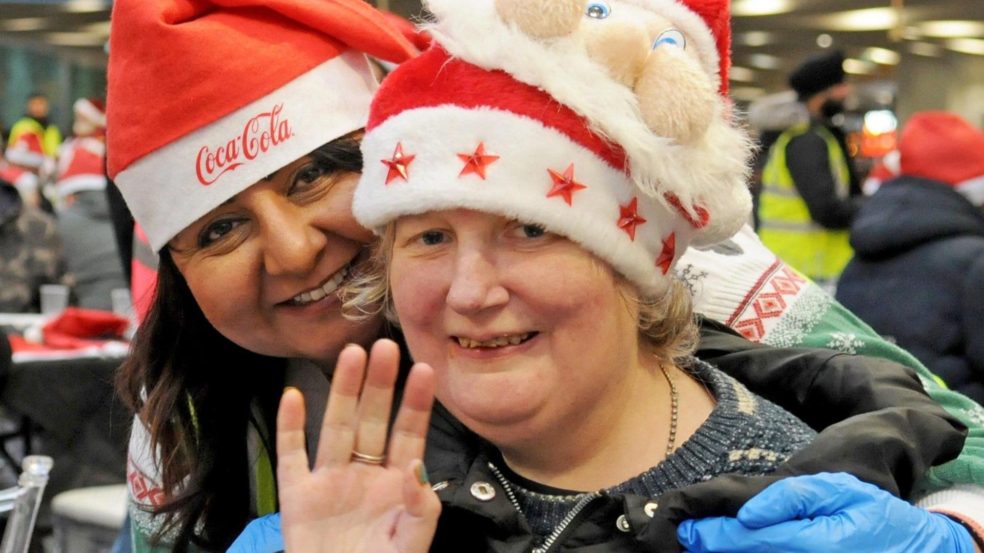 Two women are smiling while wearing santa hats and Christmas jumpers. 