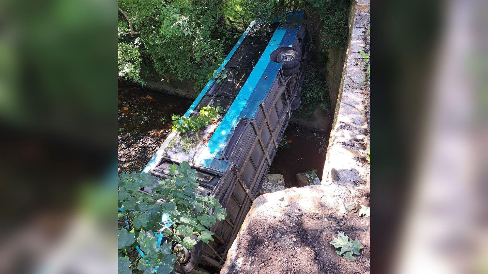 A view from above of the bus on its side in the shallow river 