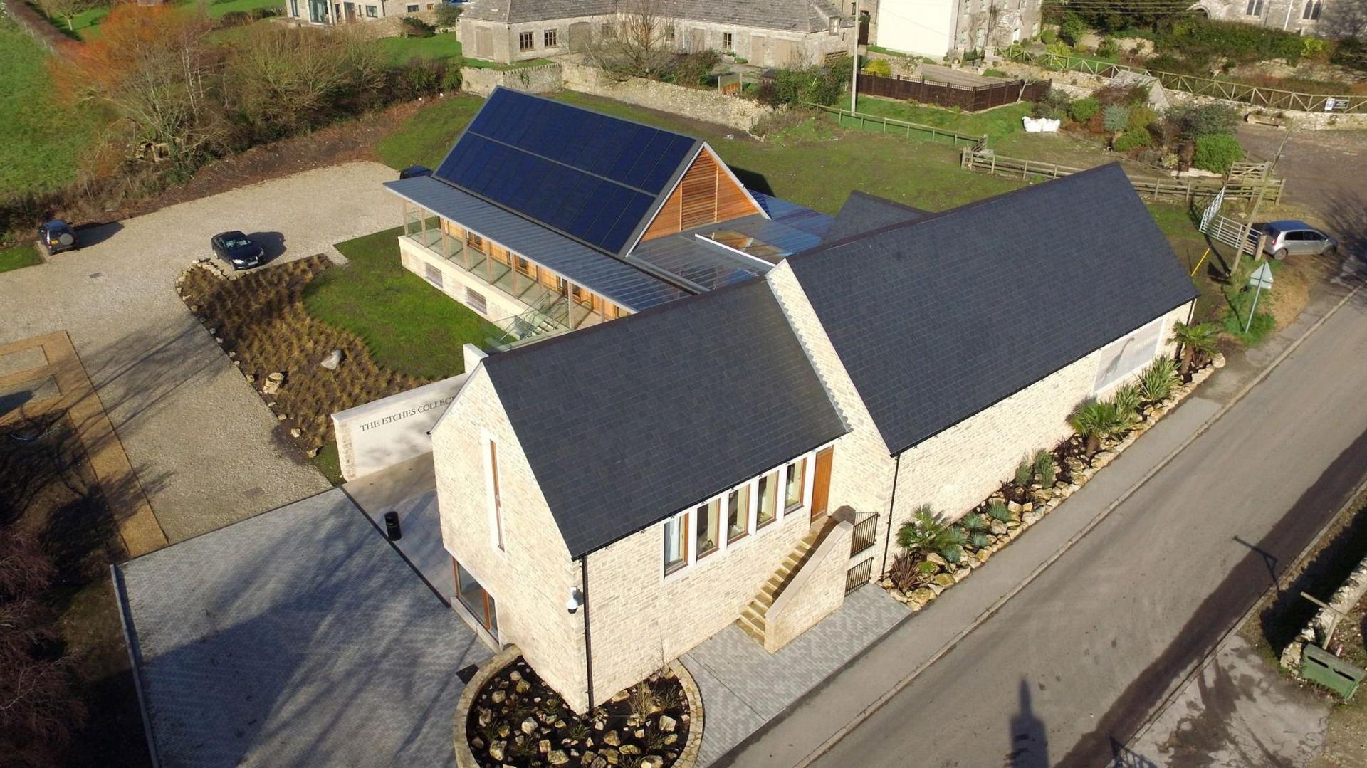 Aerial view of cream building in a 'T' shape with a slate roof and grass areas around it.