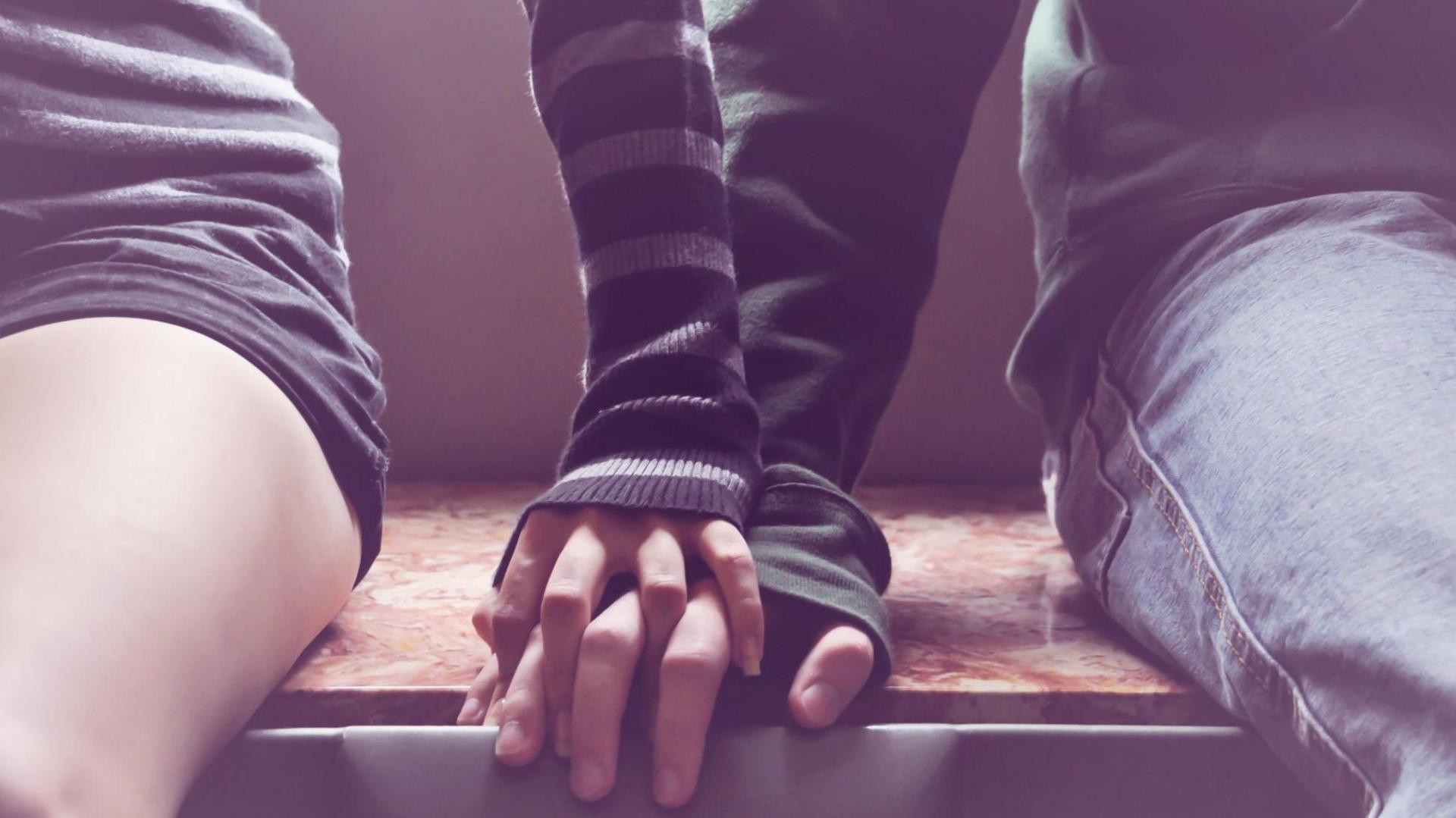 Picture of two young people one with their hand on top of the other's hand.