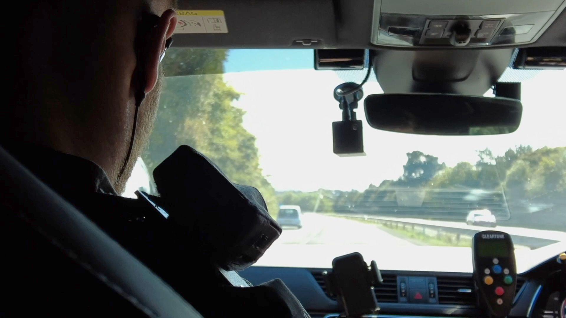 The back of a police officer's head looking out the front window of a car along a motorway