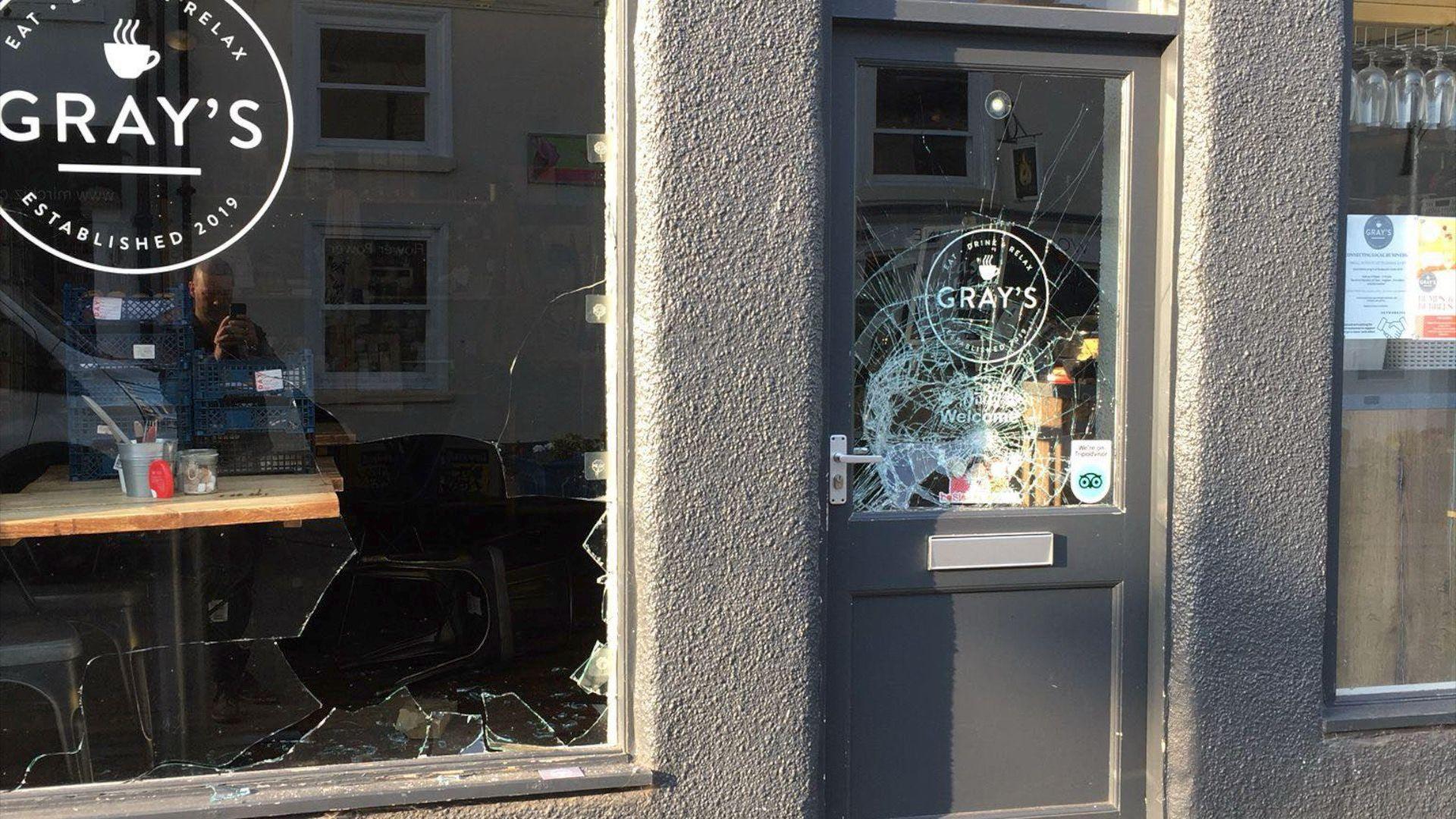 A smashed window and a broken grey door with a circular Gray's logo.