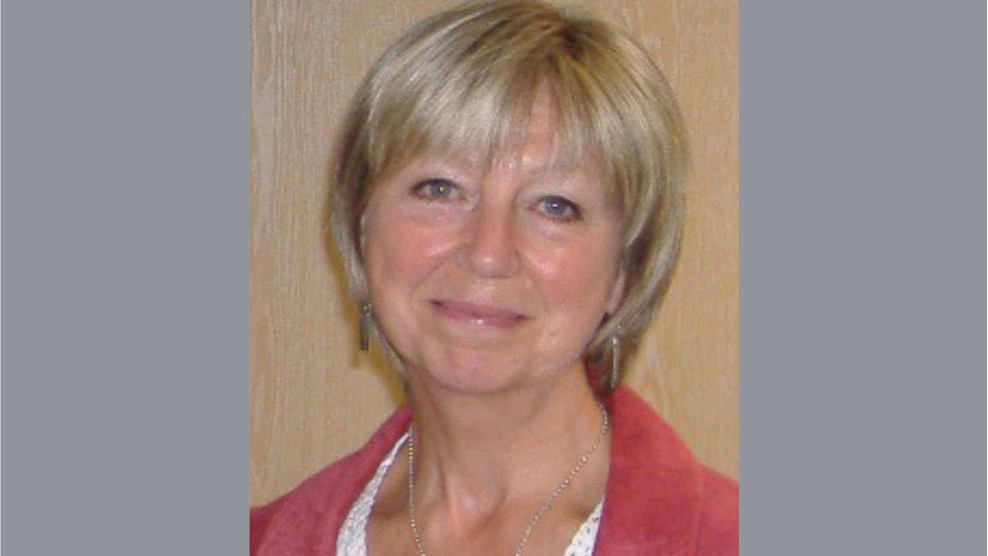 Brenda Weston in a red jacket standing against a wall