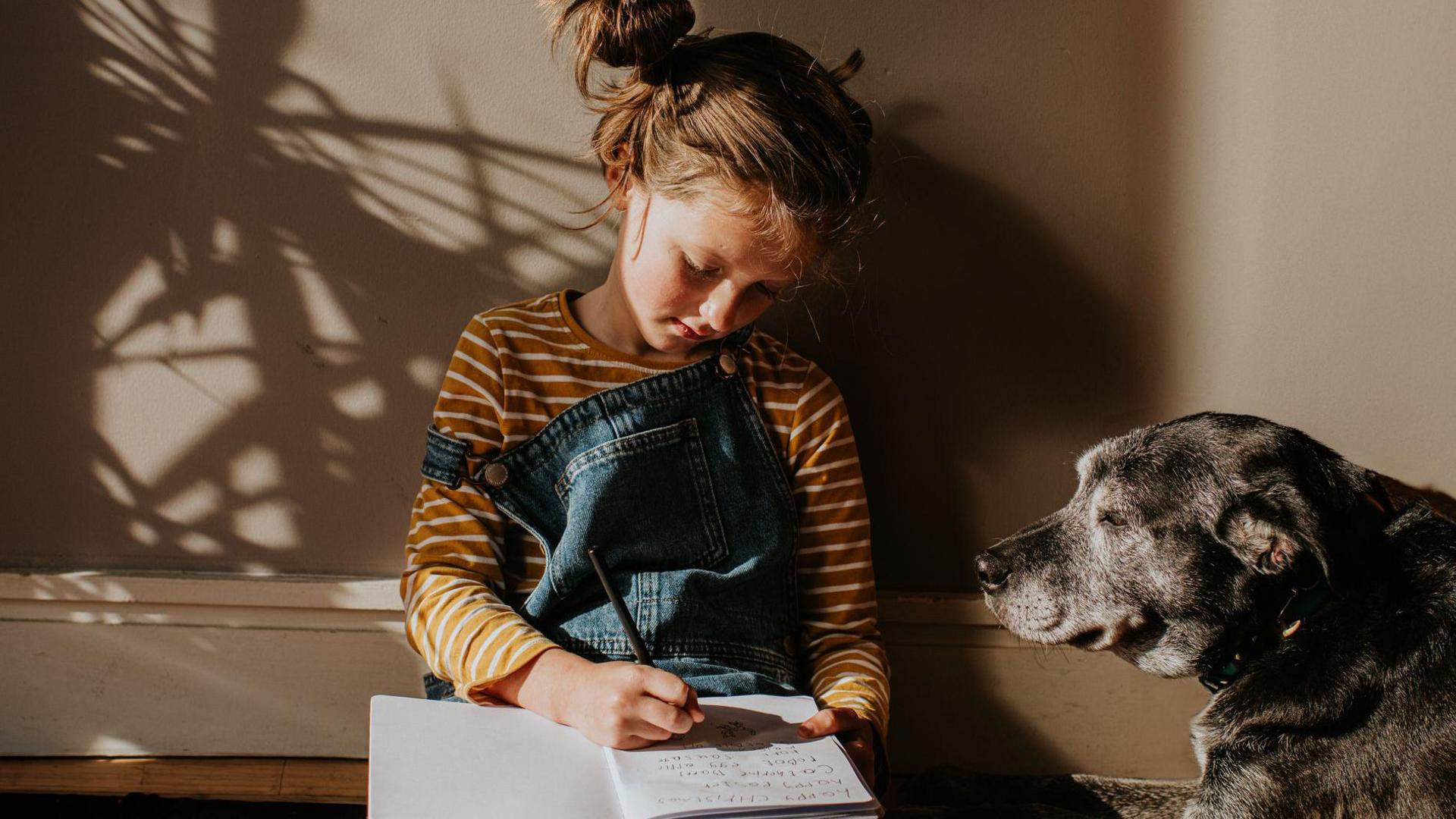 Young girl and her dog, girl is writing in notepad