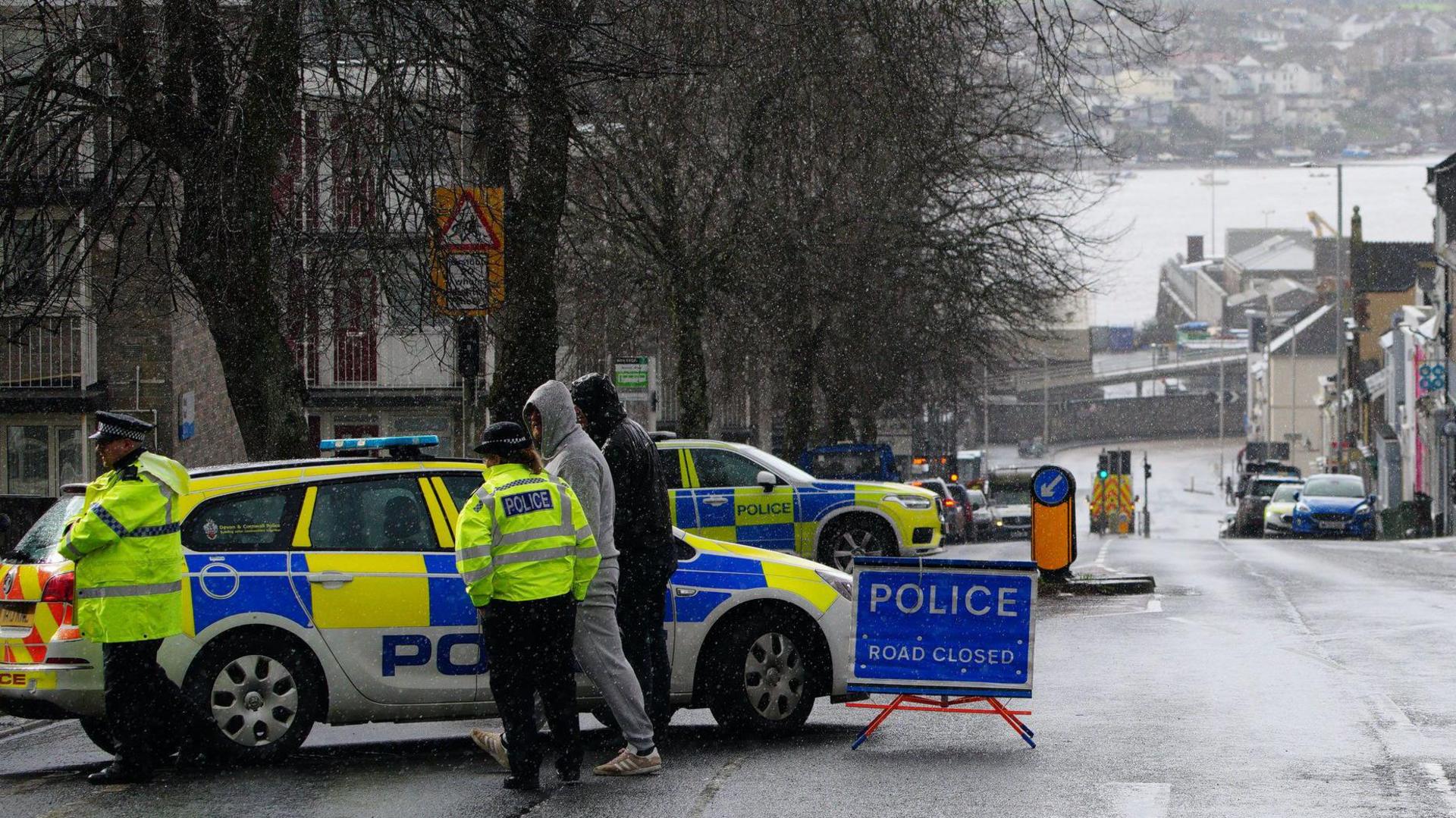 Police offers talk to residents in Plymouth in front of their police car and next to a blue sign which reads "Police. Road closed" on Friday 23 February, 2024. Residents were evacuated while a suspected World War Two bomb was removed from the garden where it was discovered and taken by military convoy to be disposed of at sea.