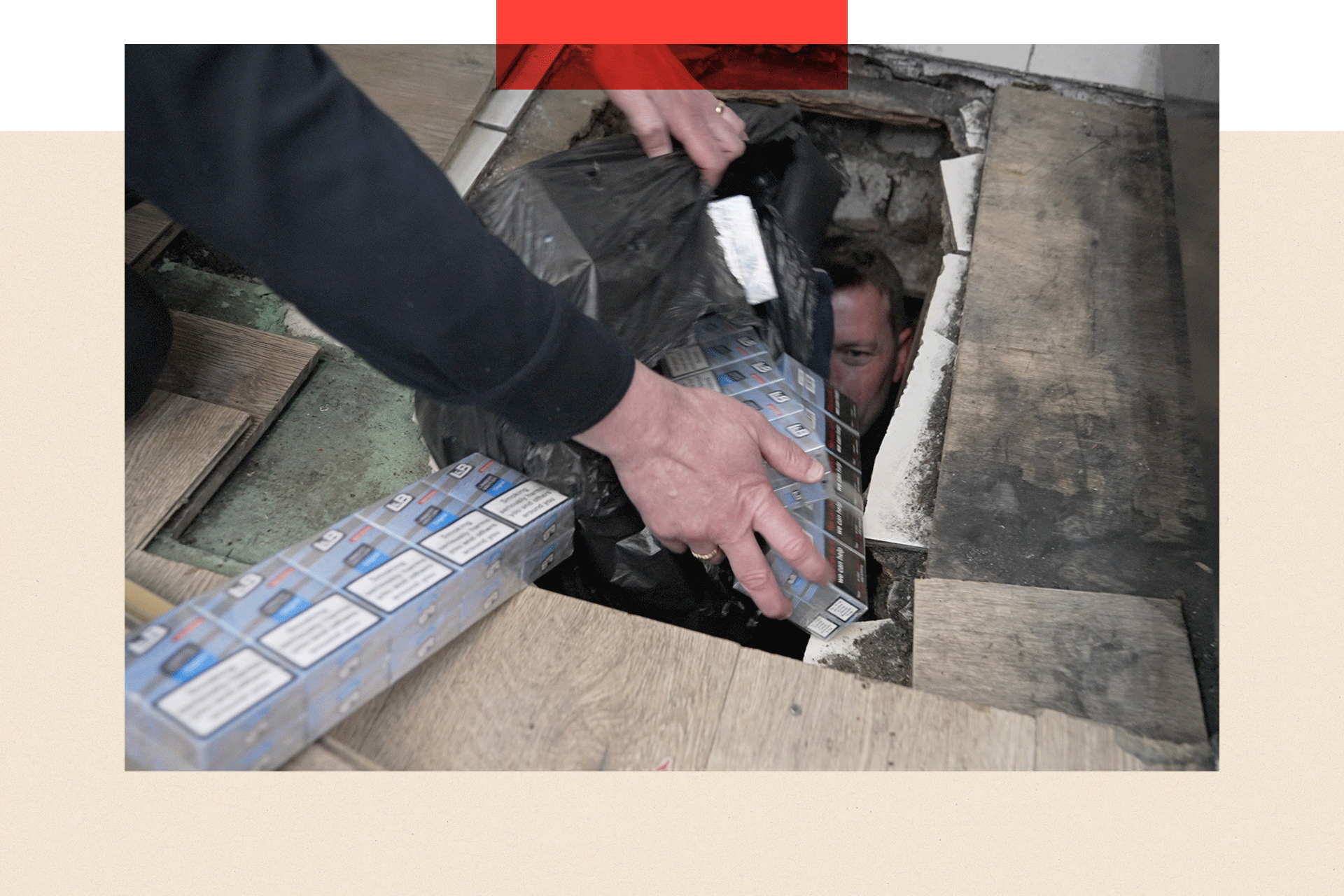 An officer bring out illegal packets of cigarettes from a hole in the floor following a raid on a corner shop