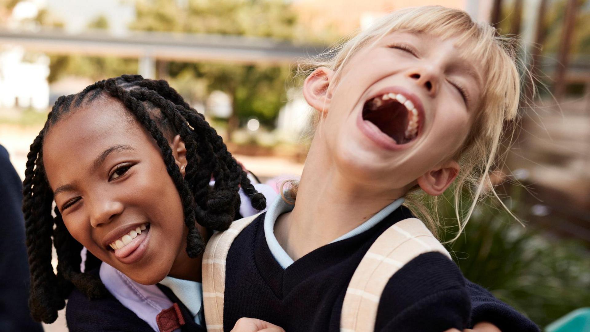 Two girls wearing school uniforms hugging and laughing together 