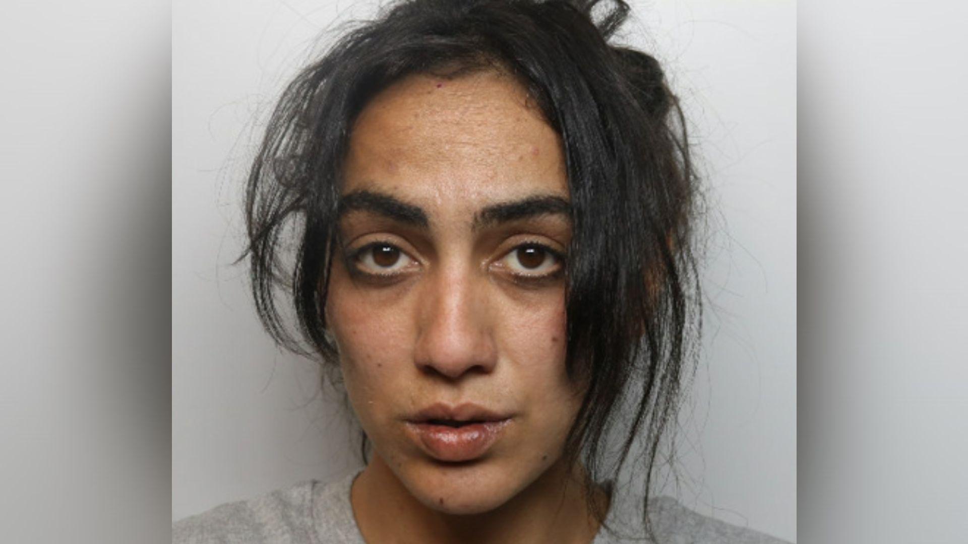 A mugshot of a woman with long black hair, partly tied back, and wearing a grey top.
