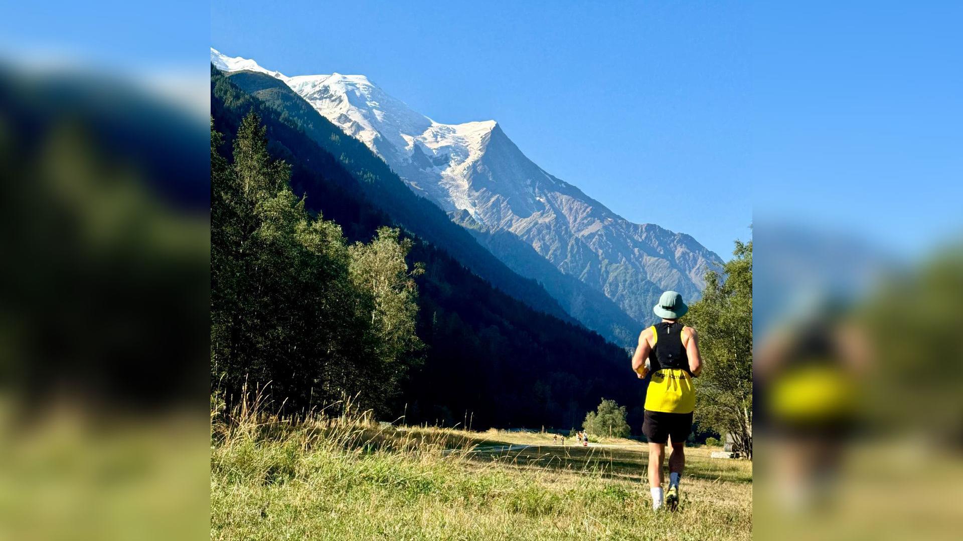 A man runs towards picturesque mountains on a sunny day. 