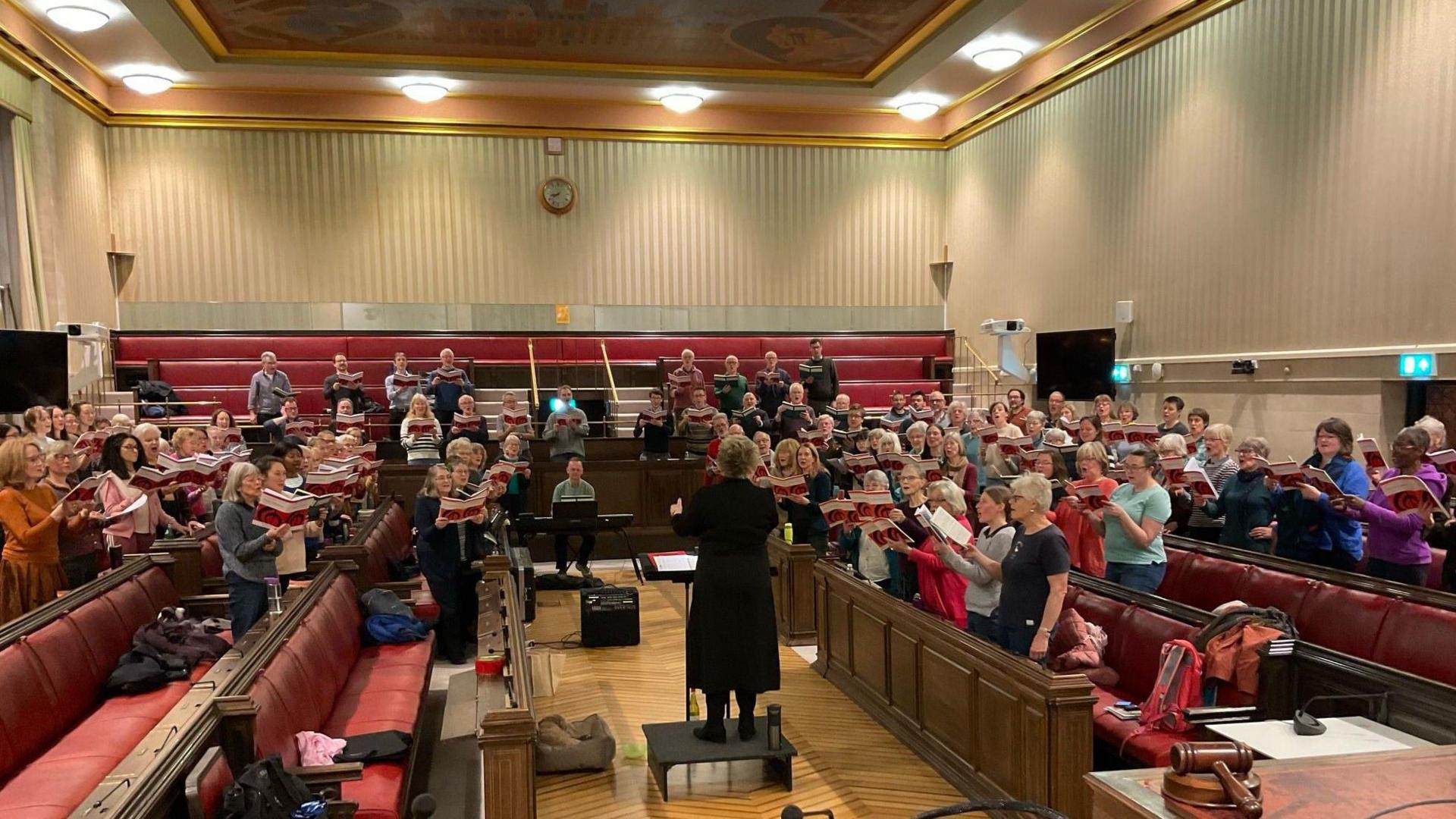 Members of the Bristol Choral Society rehearse inside the main chamber at Bristol City Council house. They are divided into different sets of singers and are holding the sheet music