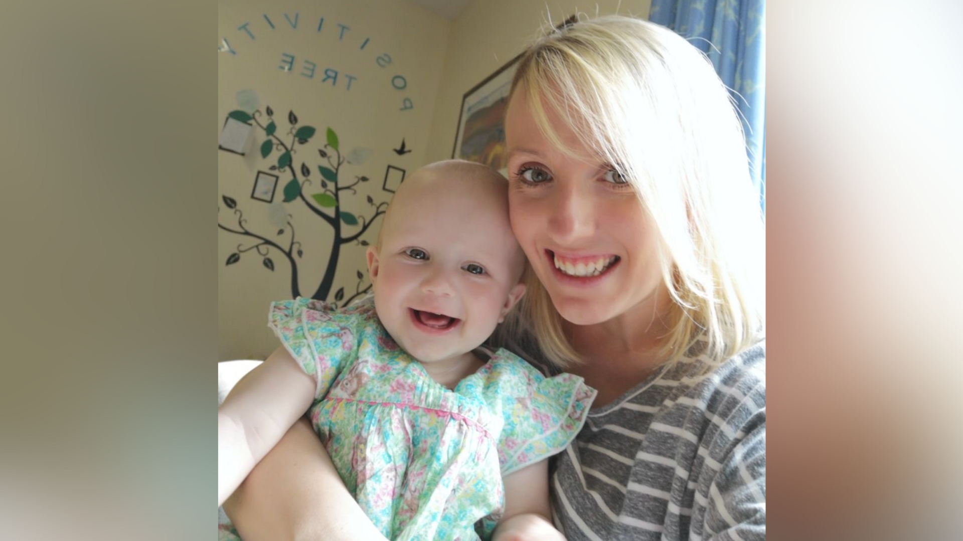 Kayleigh Avery, who has blonde hair and wears a stripy top, holds her baby, who is wearing a floral dress, while inside a hospital ward.