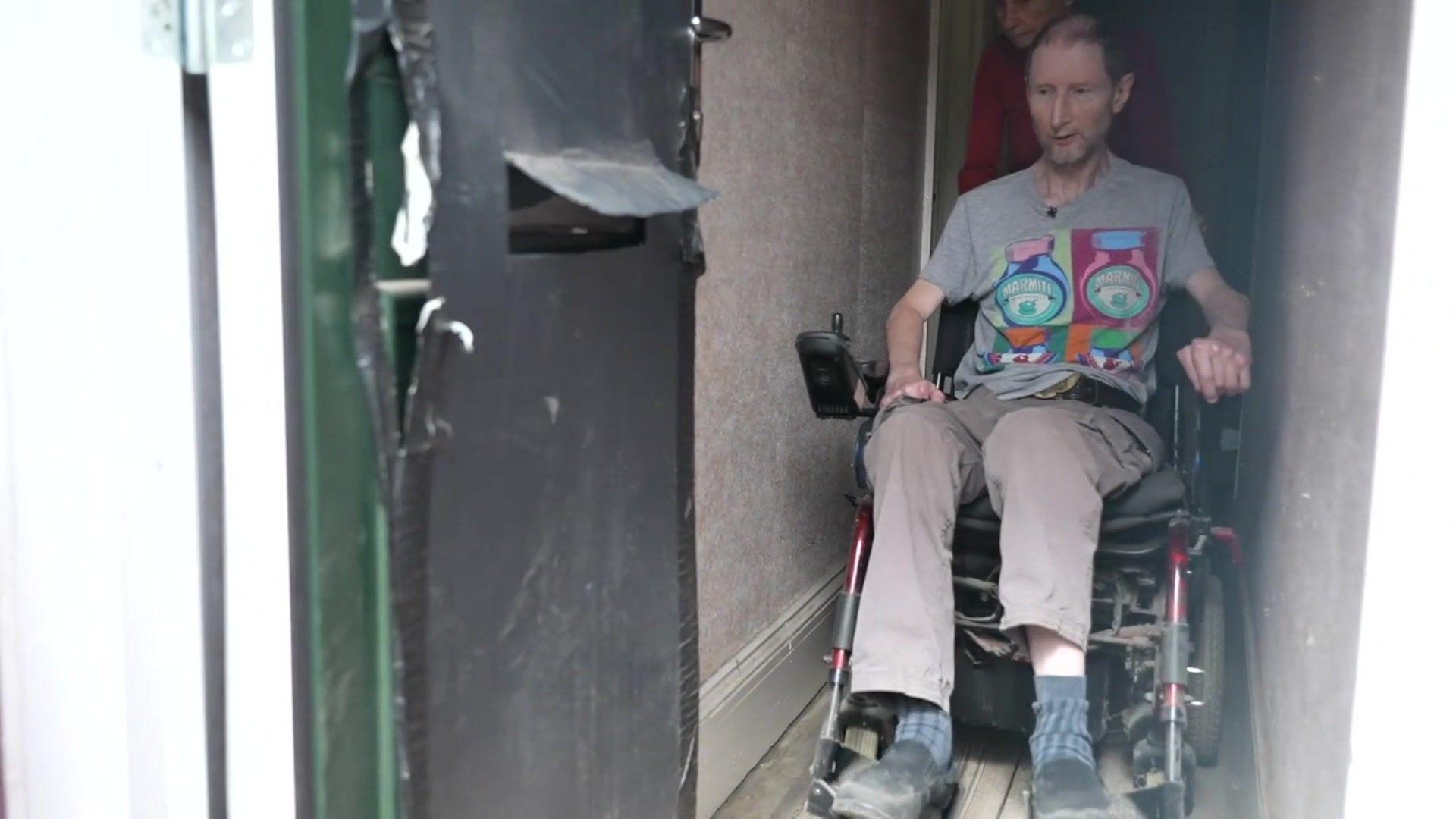 Peter Jeapes in his front hallway demonstrating how his electric wheelchair won't fit through his front door