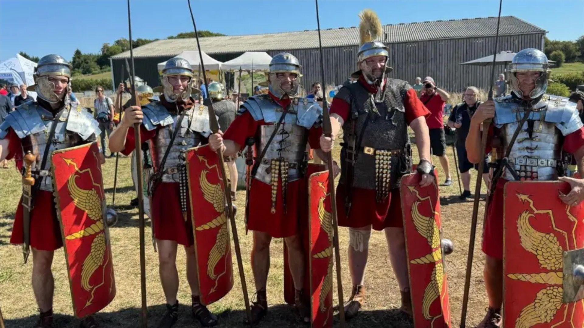A group of people dressed in Roman attire with helmets and shields looking into the camera.