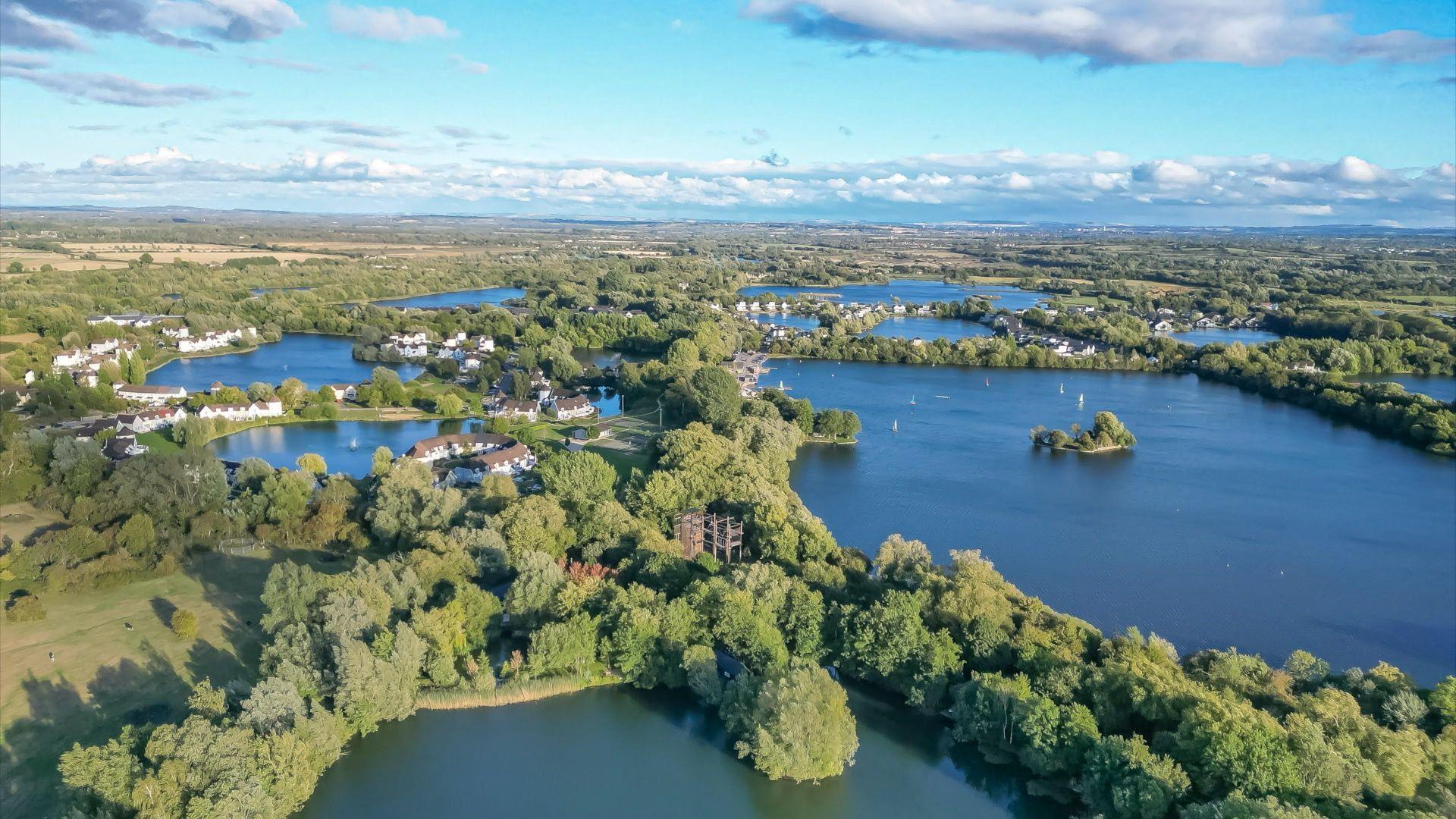 Aerial still of South Cerney with lots of green trees and lake waters.