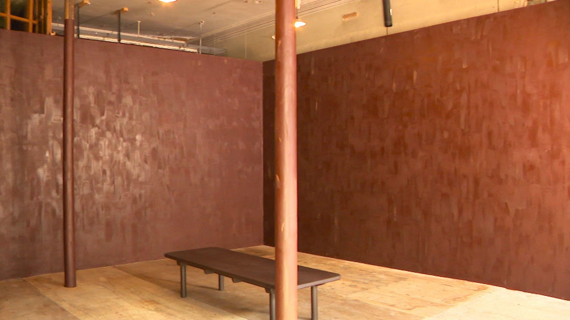 An empty room with just a bens. The walls are painted with dark chocolate and the pillars are also covered in chocolate.