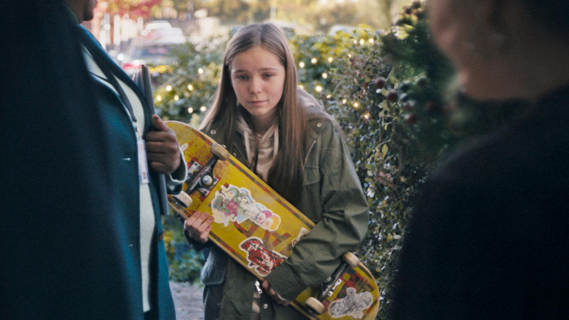 A girl with skateboard looks on