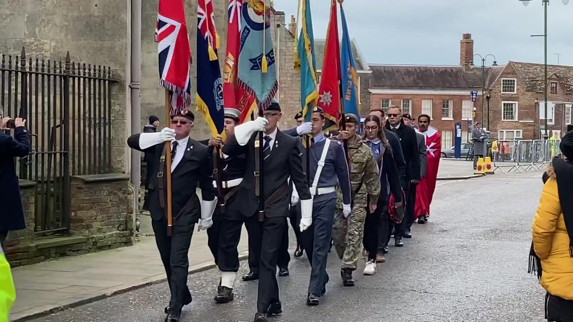 Standard bearers with standards raised marching past an old building in Kings Lynn