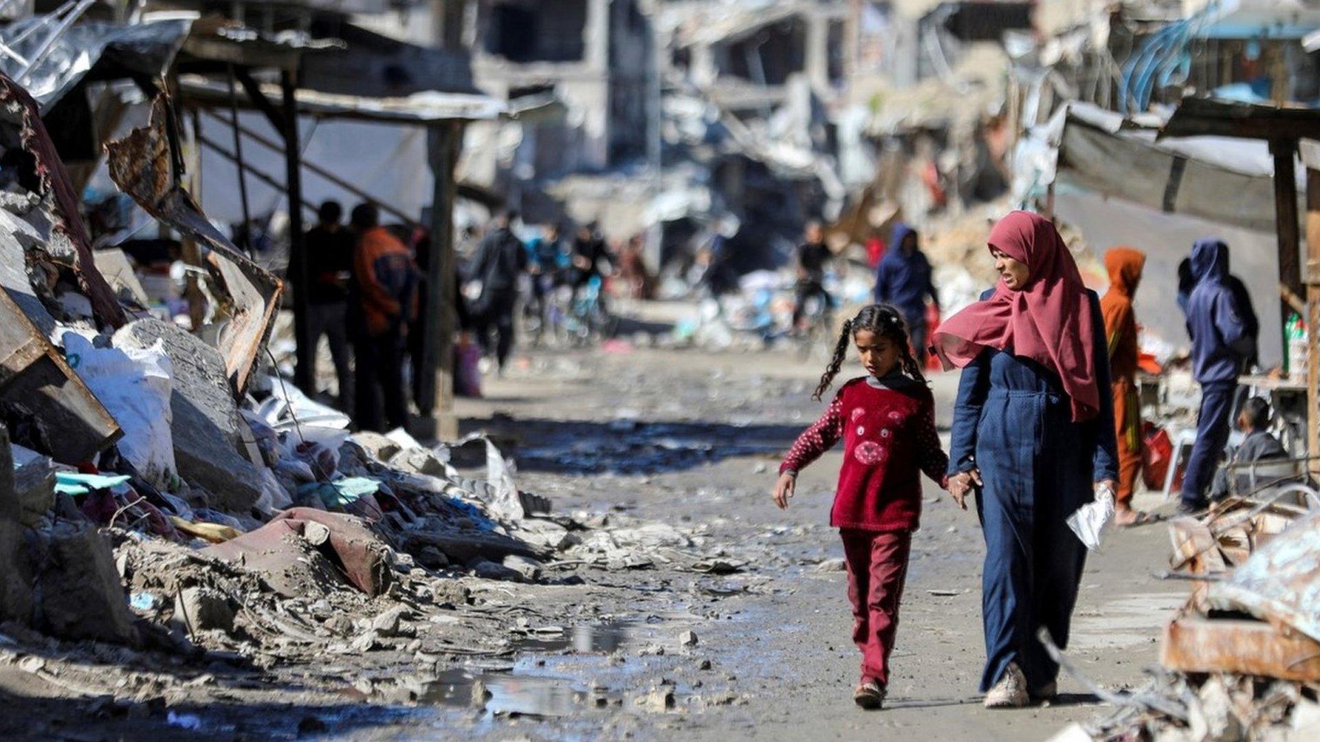 Palestinians walk past destroyed buildings in Gaza City (20 March 2024)