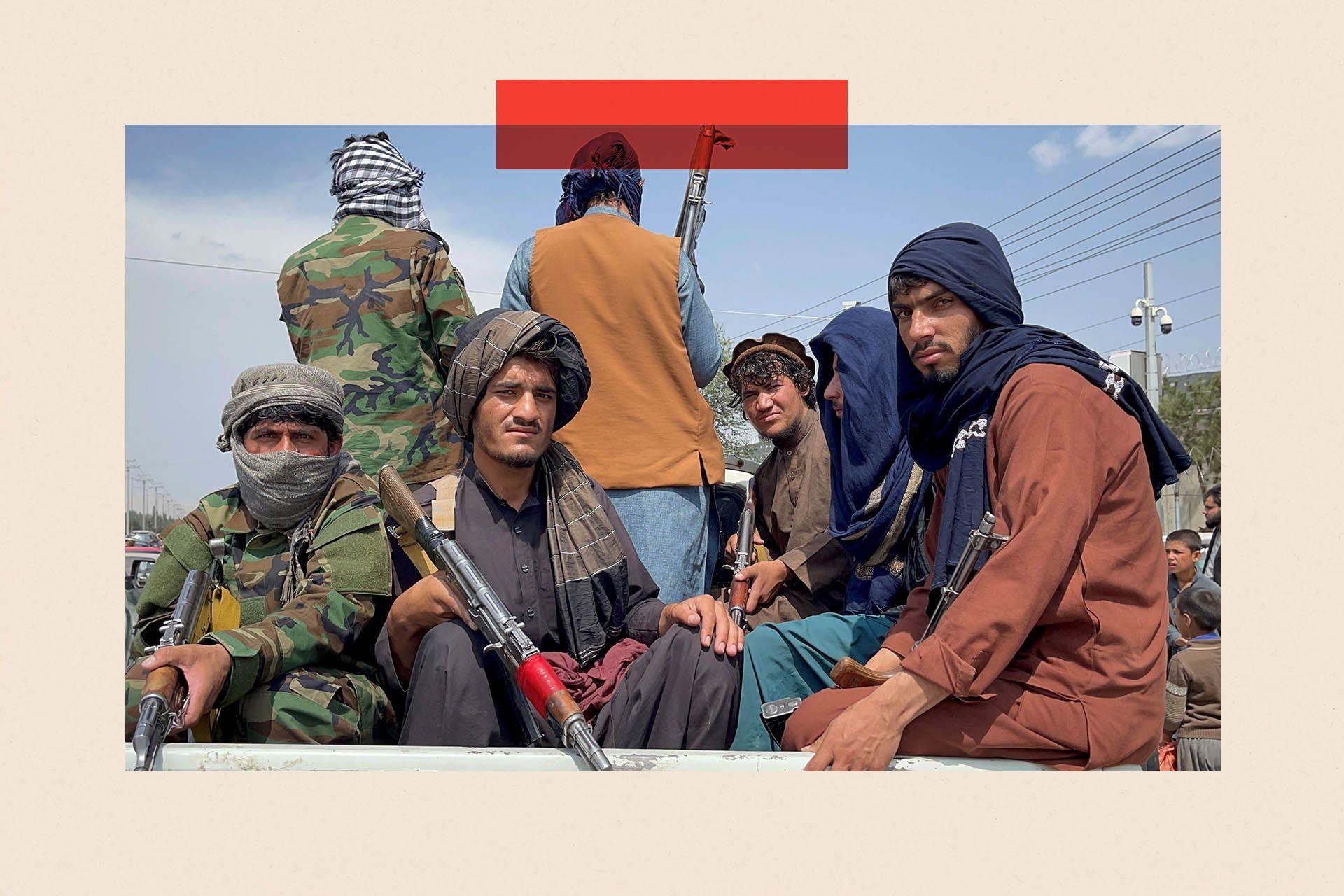 Taliban fighters in traditional clothes and holding weapons sit on the back of an open-top vehicle 