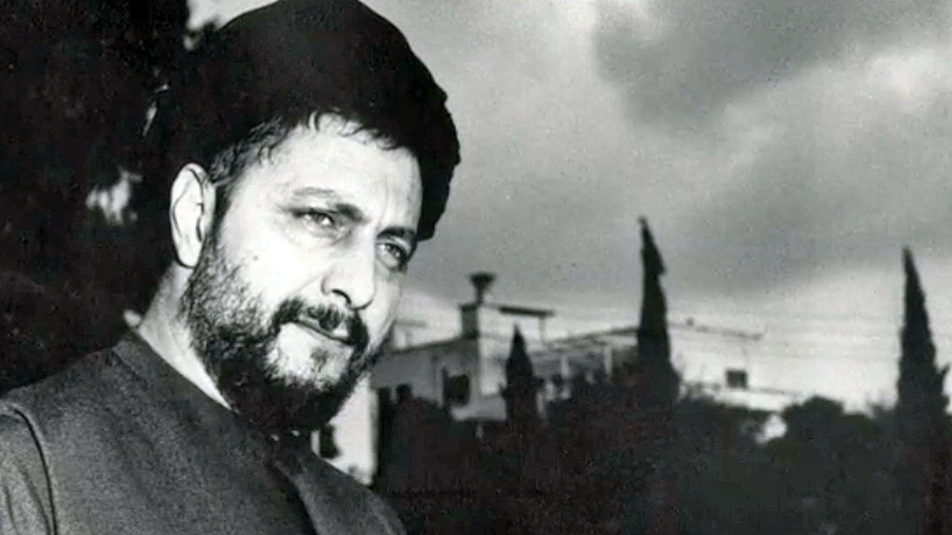 A black and white image of Musa al-Sadr. He has a beard, is wearing a hat and is looking thoughtful. There are trees and buildings in the background.