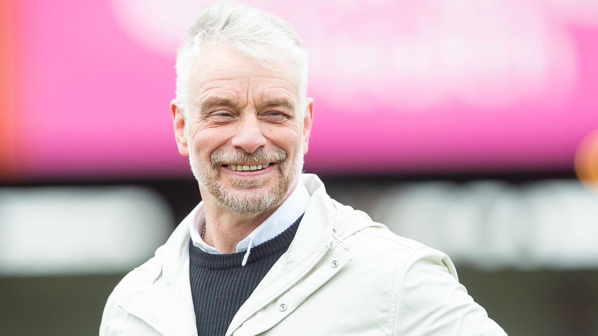 Brian Noble smiles as he takes in the surroundings of a rugby league ground in his coat.