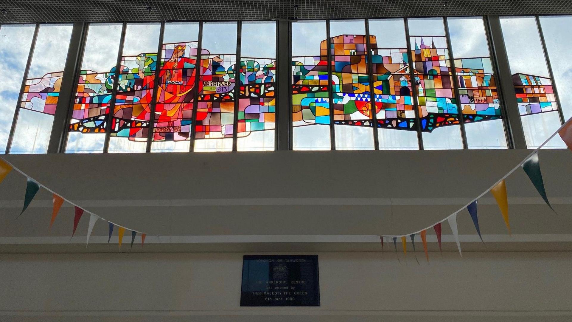 A stained glass window, depicting a colourful range of abstract imagery connected with the town of Tamworth - including Lady Aethelflaed, local landmarks and the Mercian flag.