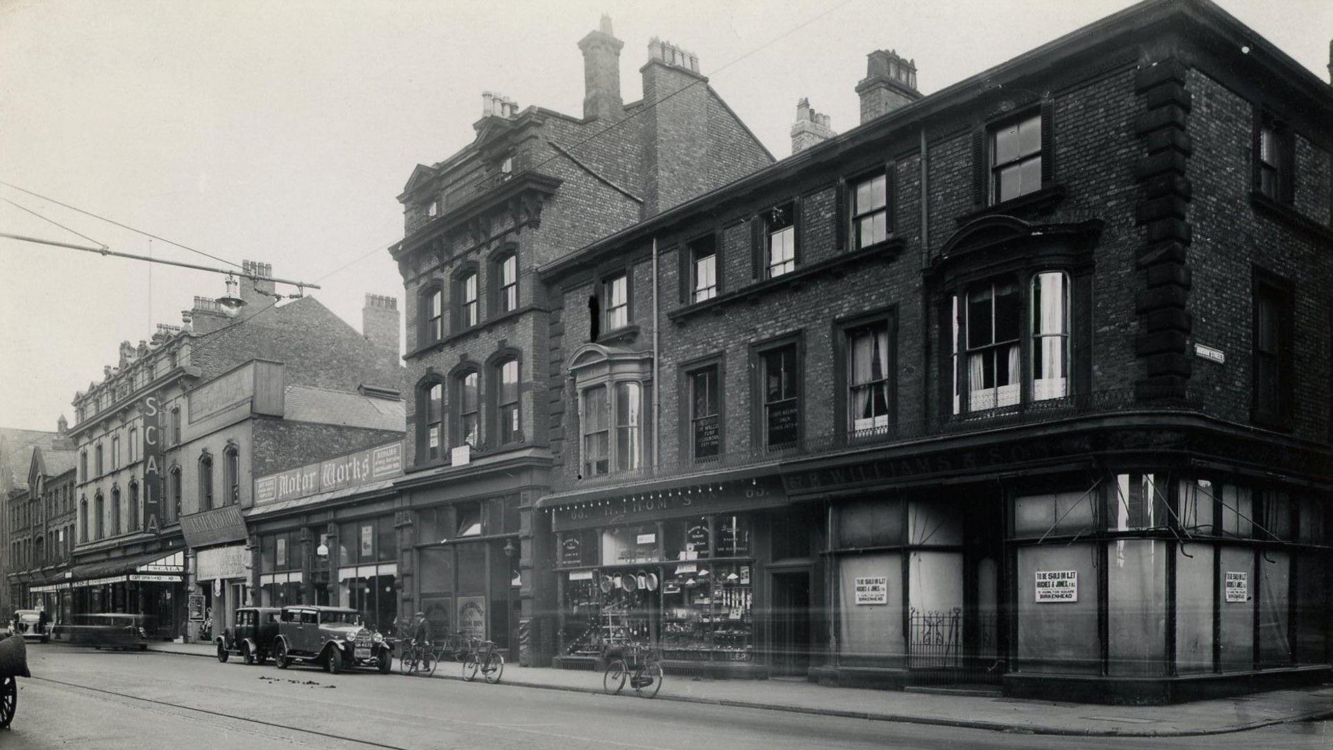 Black and white image of Argyle Street looking towards the Scala Cinema. There are old motor cars and bicycles parked on the side of the street