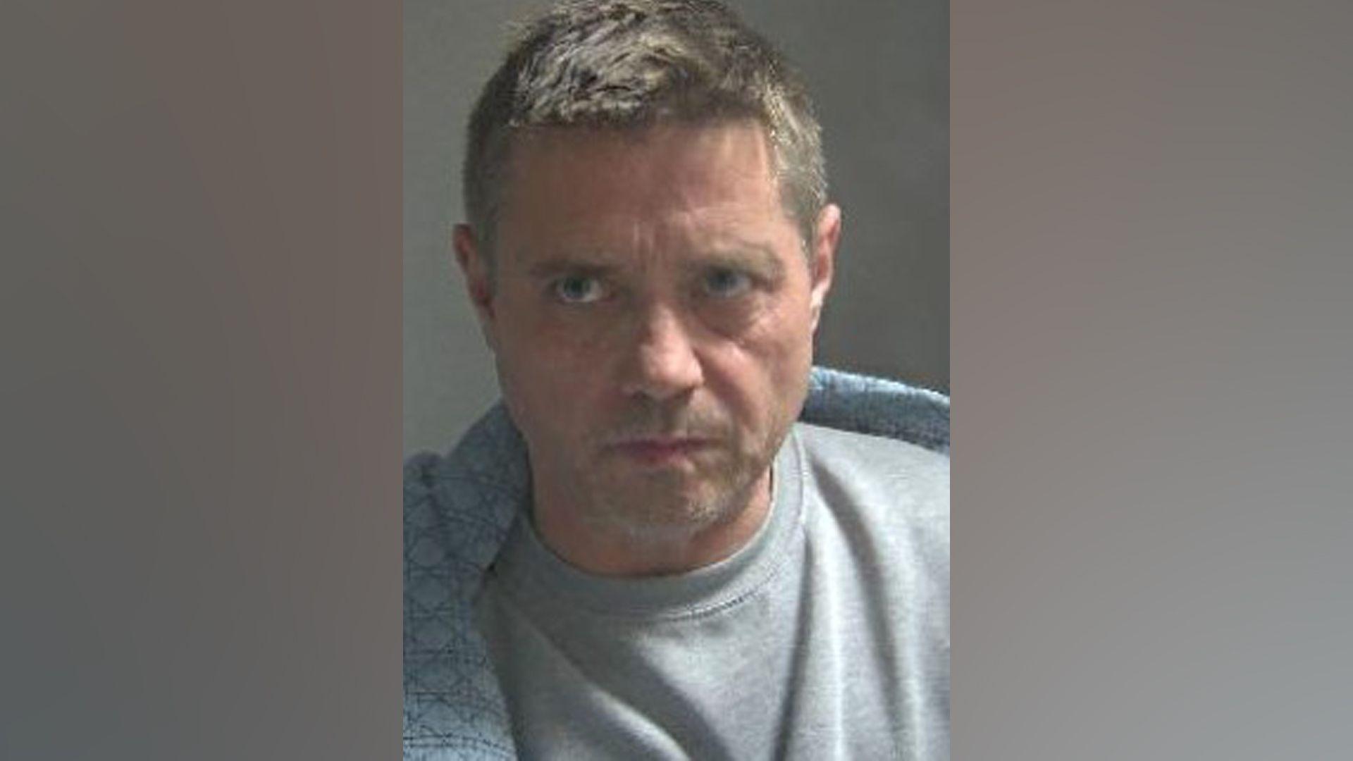 A mug shot of John Alford wearing a grey T-shirt
