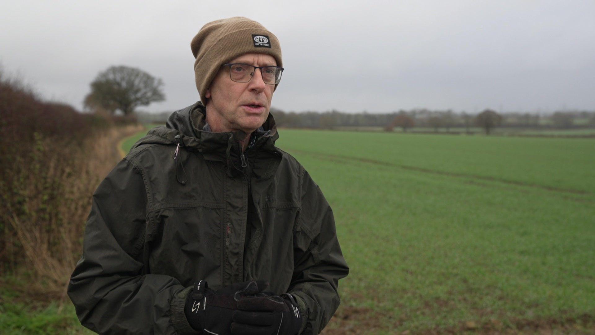 Philip Martin, who is wearing a brown beanie hat and a dark green jacket. He has glasses.