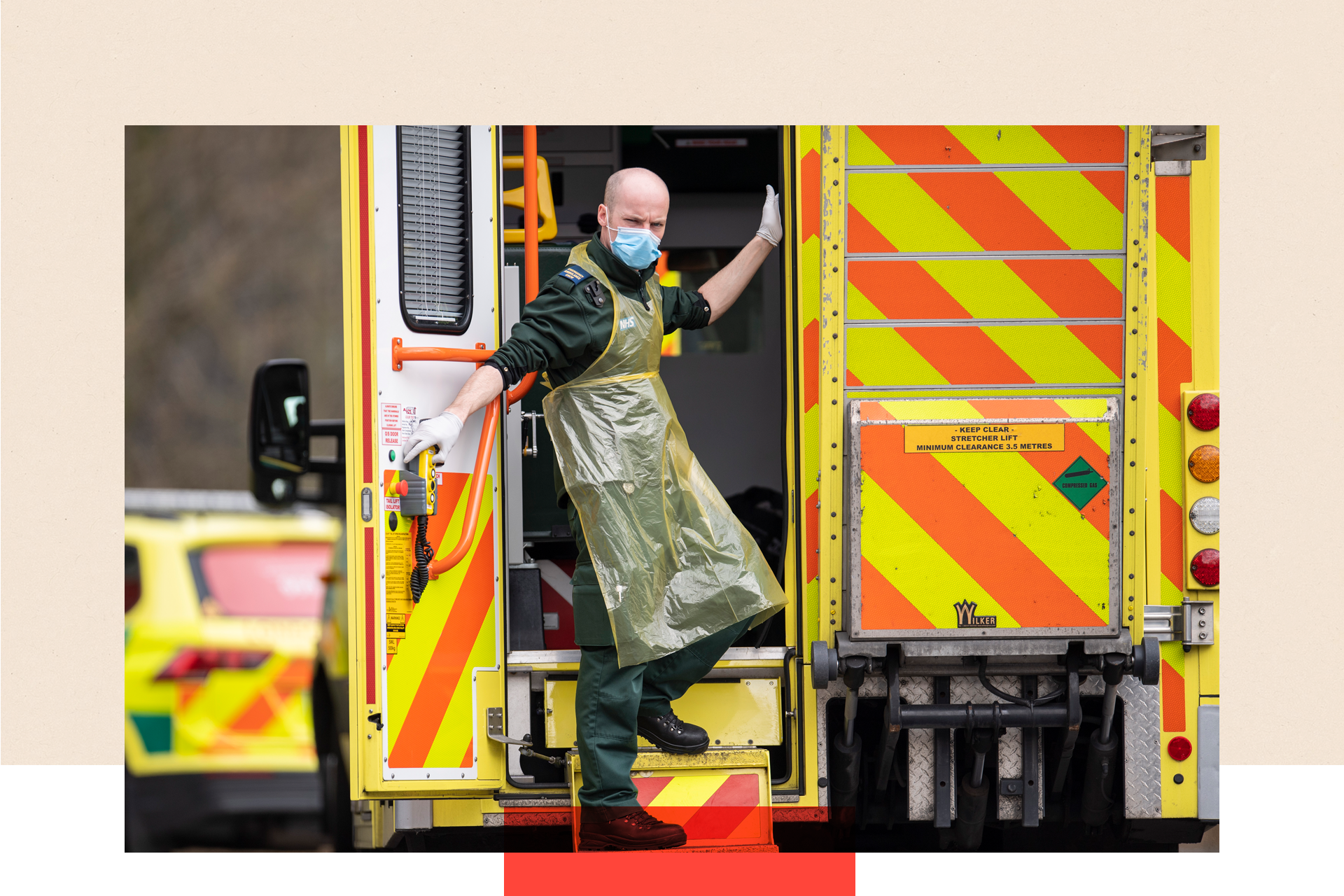 An ambulance worker in the back of an ambulance outside a hospital, wearing a mask.