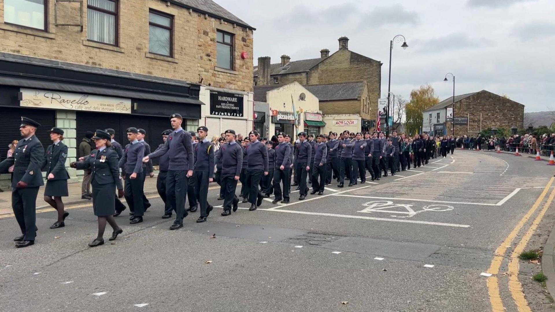 Men and women dressed in Navy blue parade along a closed high street.