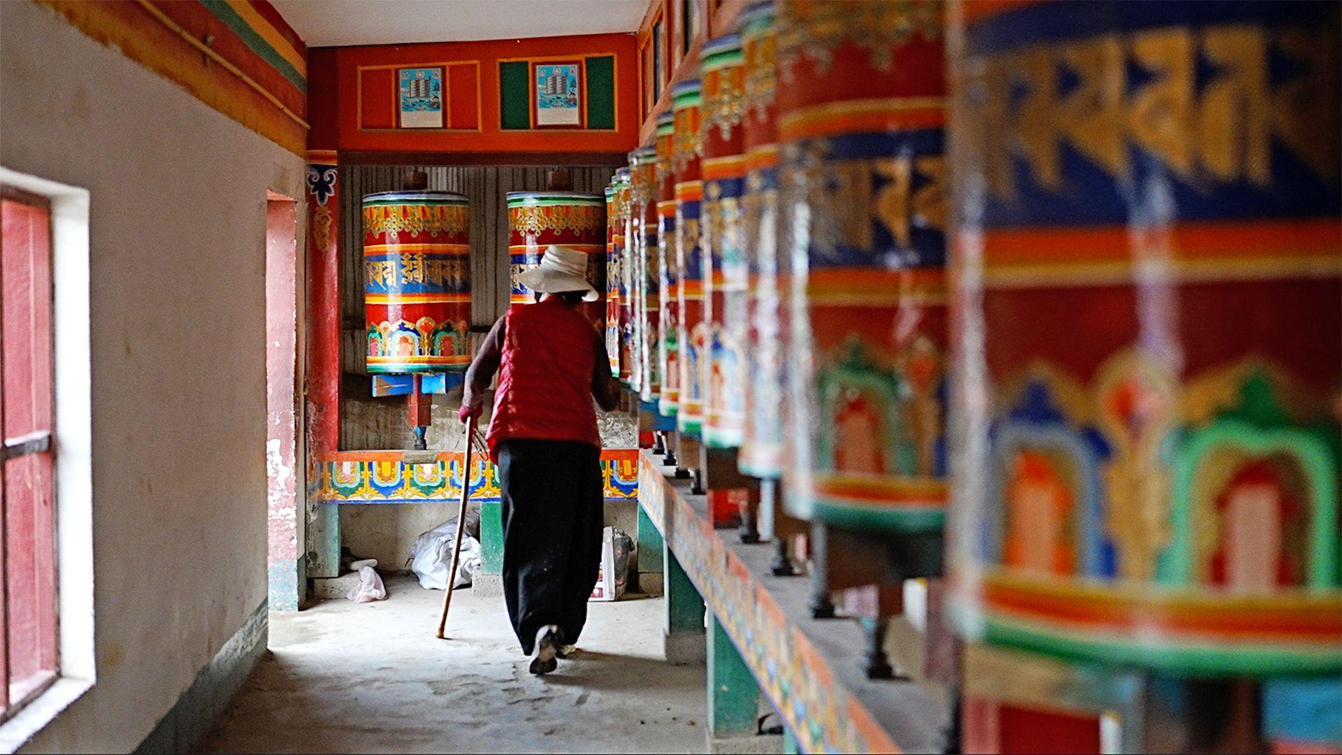 A woman walks past colourful prayer wheels depicting murals from the Buddha's life inside the Kirti monastery