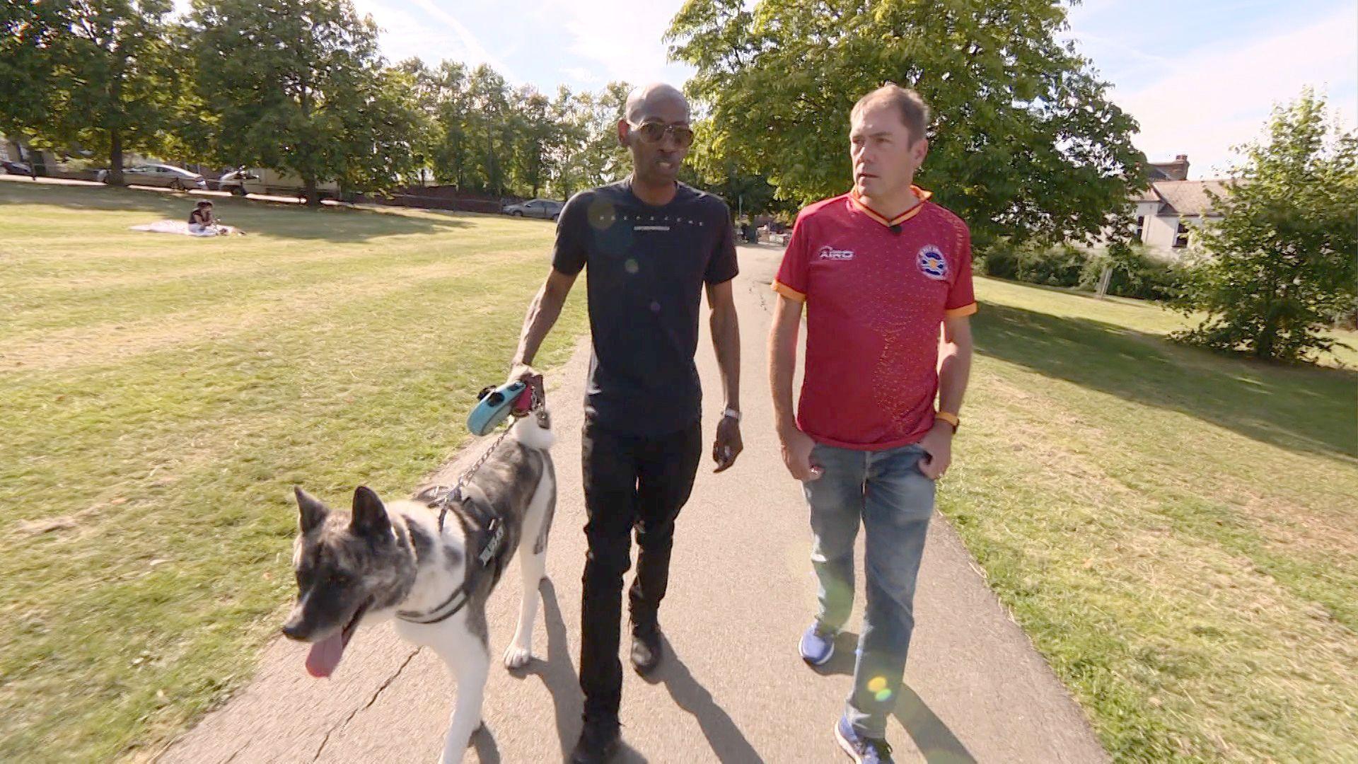 One man walks alongside another walking a dog