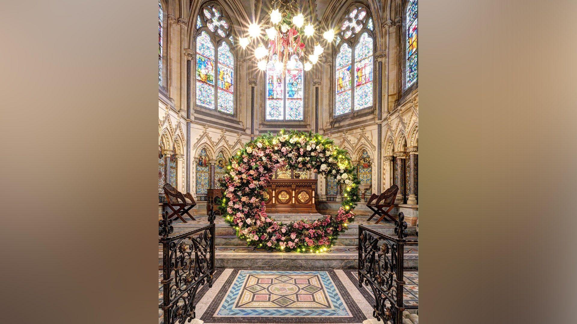 A large wreath stands on the steps in front of a chapel.