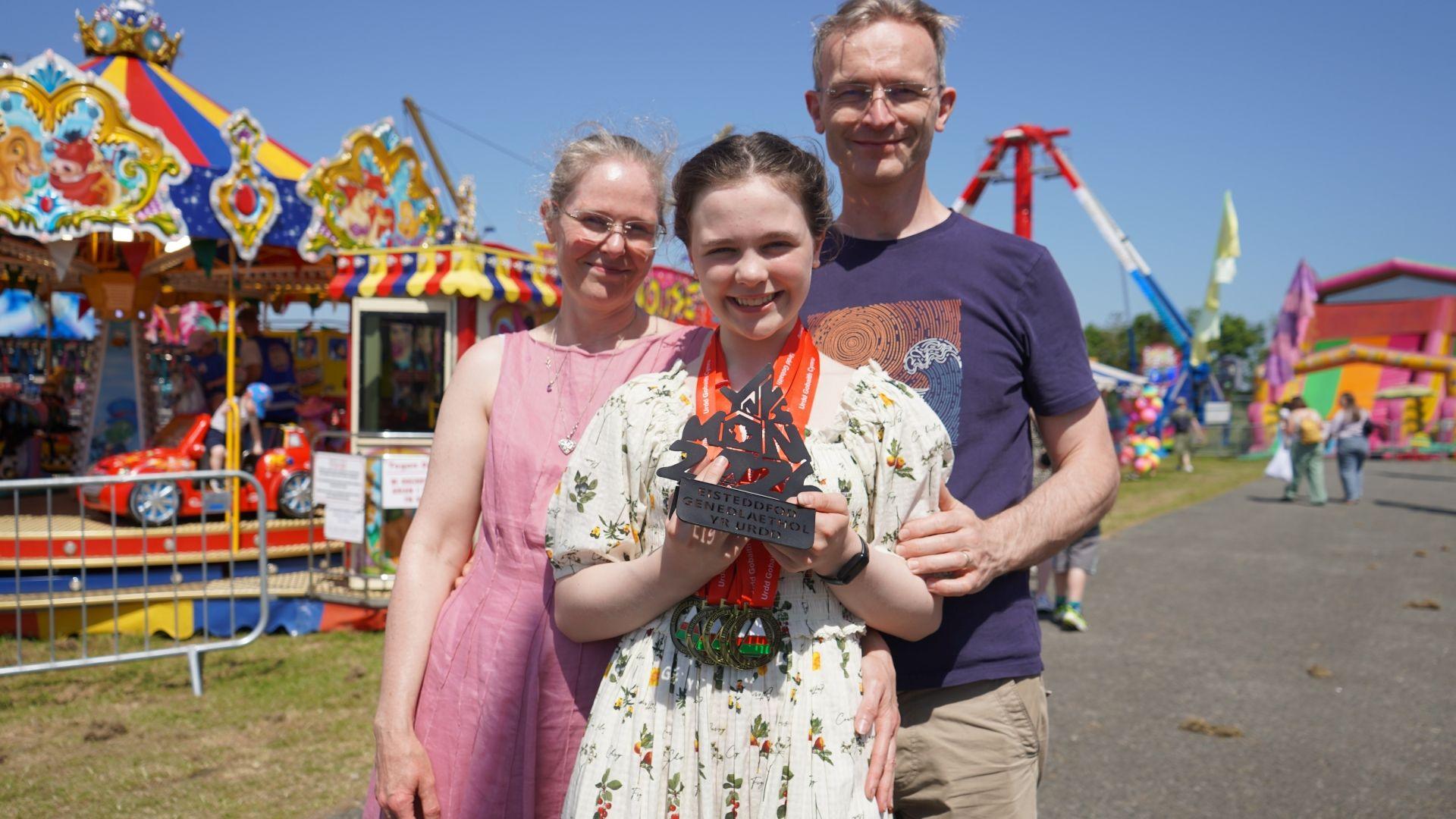 Ella o'r Drenewydd gyda'i rhieni balch. Mae Ella wedi ennill pump o fedalau gwobr gyntaf gan gynnwys dod yn gyntaf am greu pyped, gemwaith, ffasiwn creu gwefan ac am ei phroisect gwyddoniaeth. Hi hefyd sydd wedi cipio gwobr goffa Alwyn R. Owens sy'n cael ei gyflwyno'n flynyddol i wyddonydd ifanc addawol.