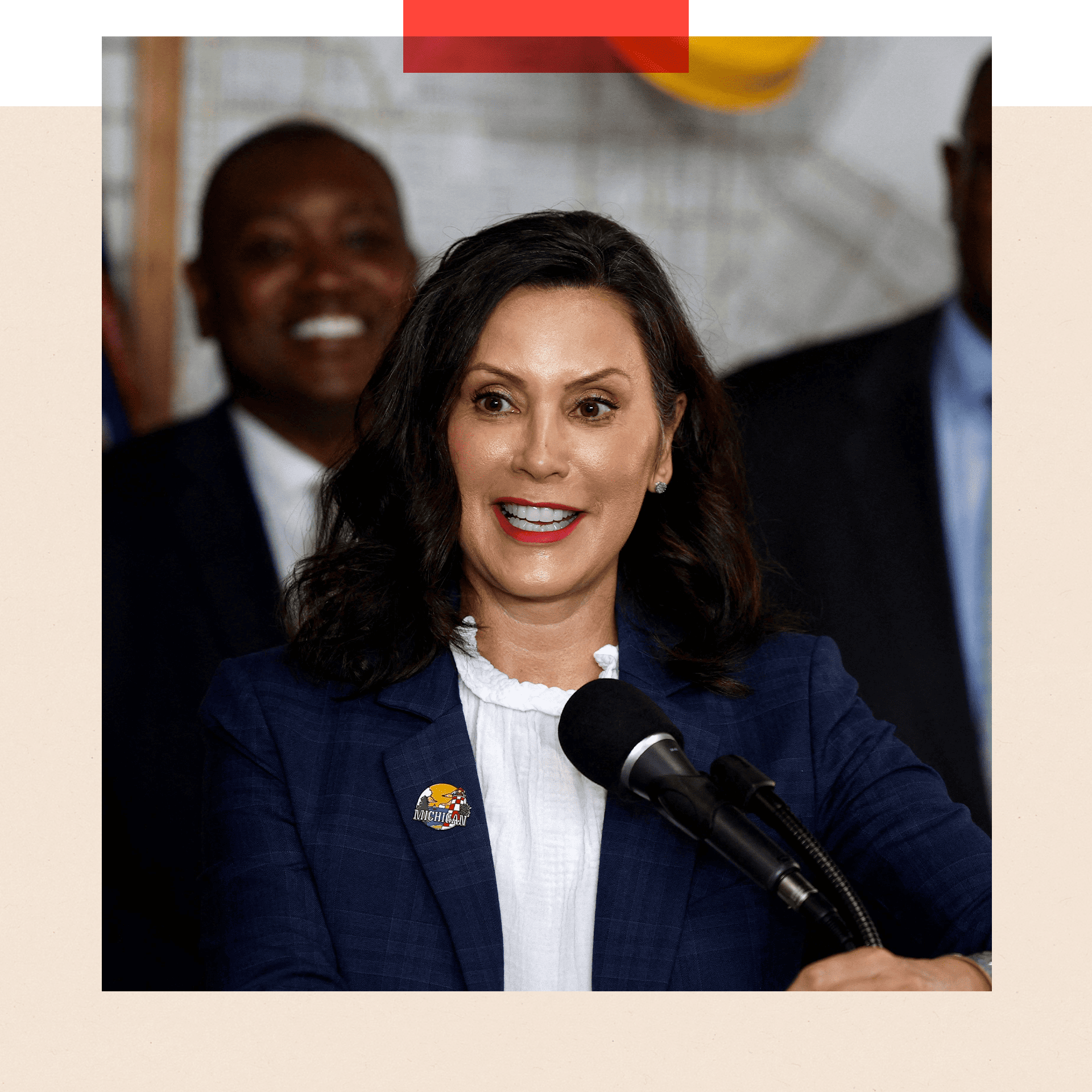 Gretchen Whitmer speaks into a microphone. She is wearing a white short and a navy blue jacket