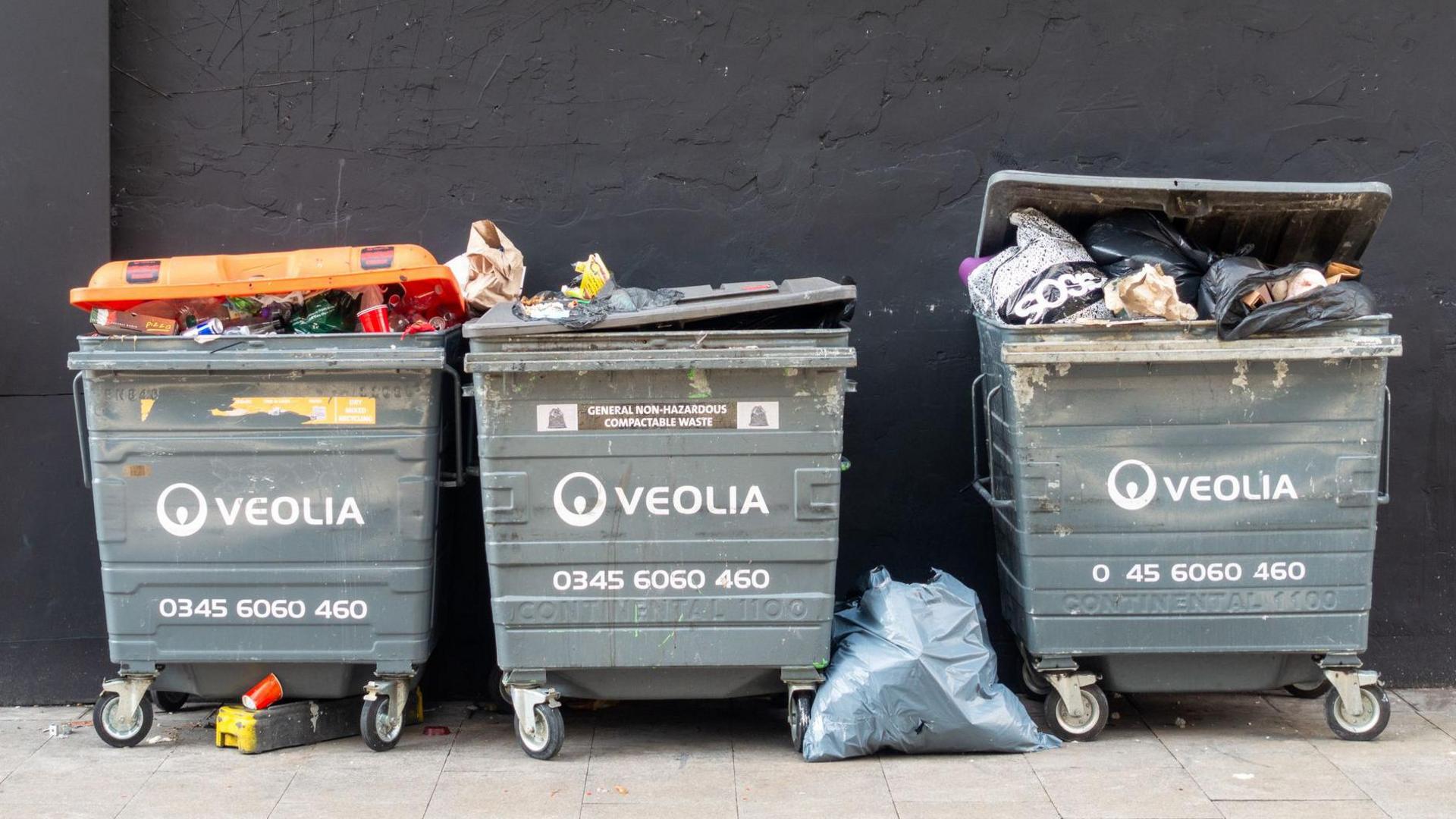 Three large grey industrial waste bins in a row with words Veolia written on each bin